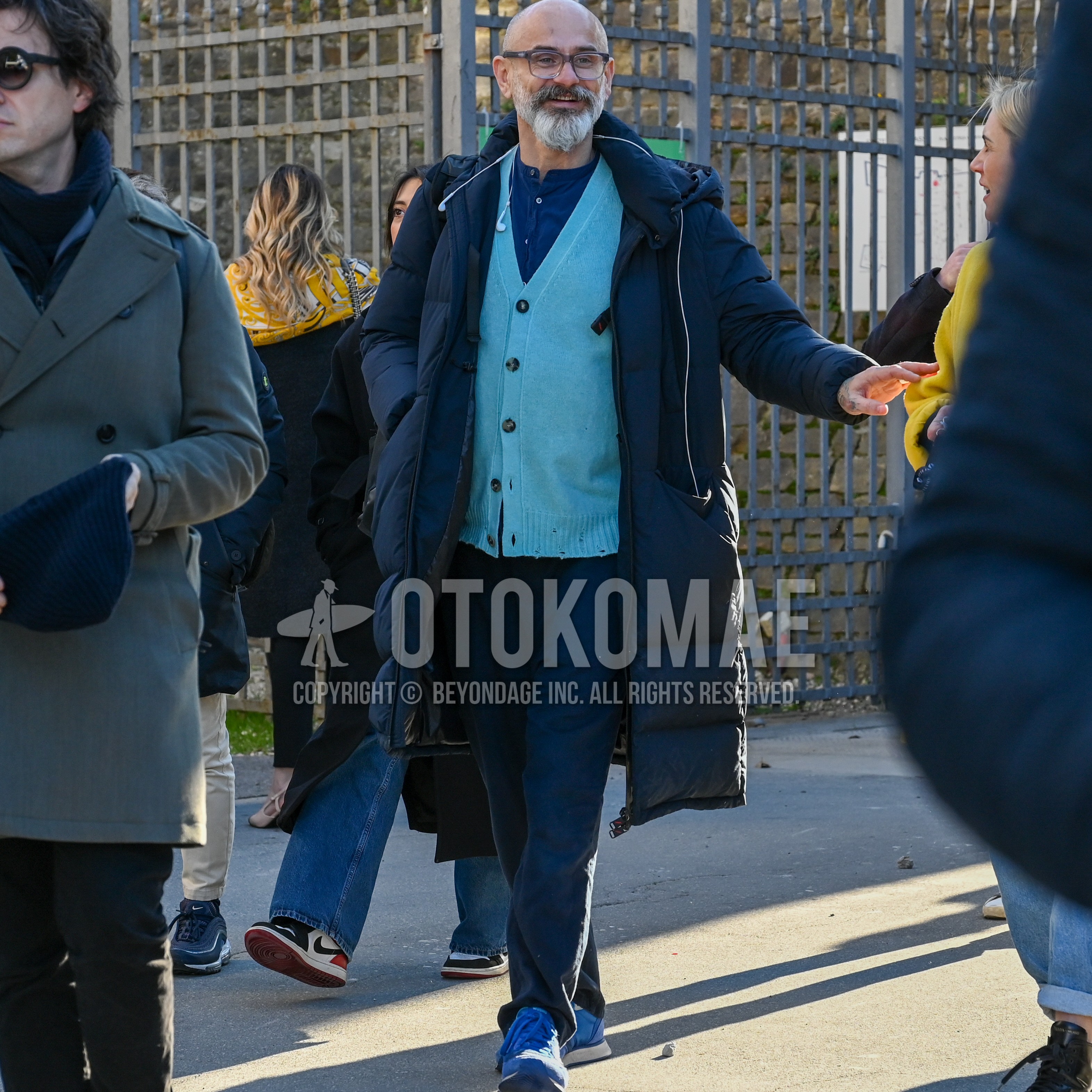 Men's autumn winter outfit with gray eyewear glasses, navy plain hooded coat, light blue plain cardigan, navy plain shirt, navy plain chinos, blue low-cut sneakers.