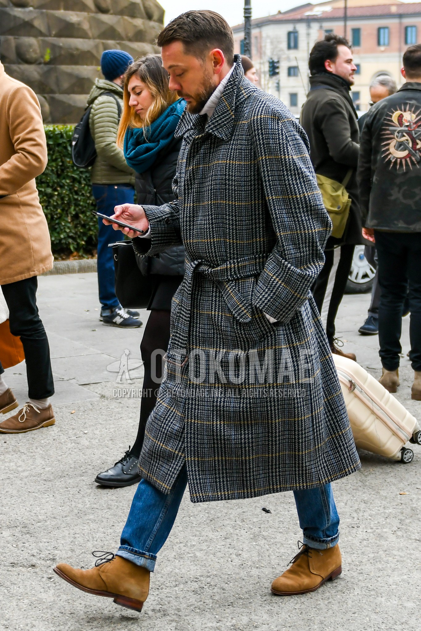 Men's autumn winter outfit with gray check belted coat, white plain turtleneck knit, blue plain denim/jeans, beige chukka boots.
