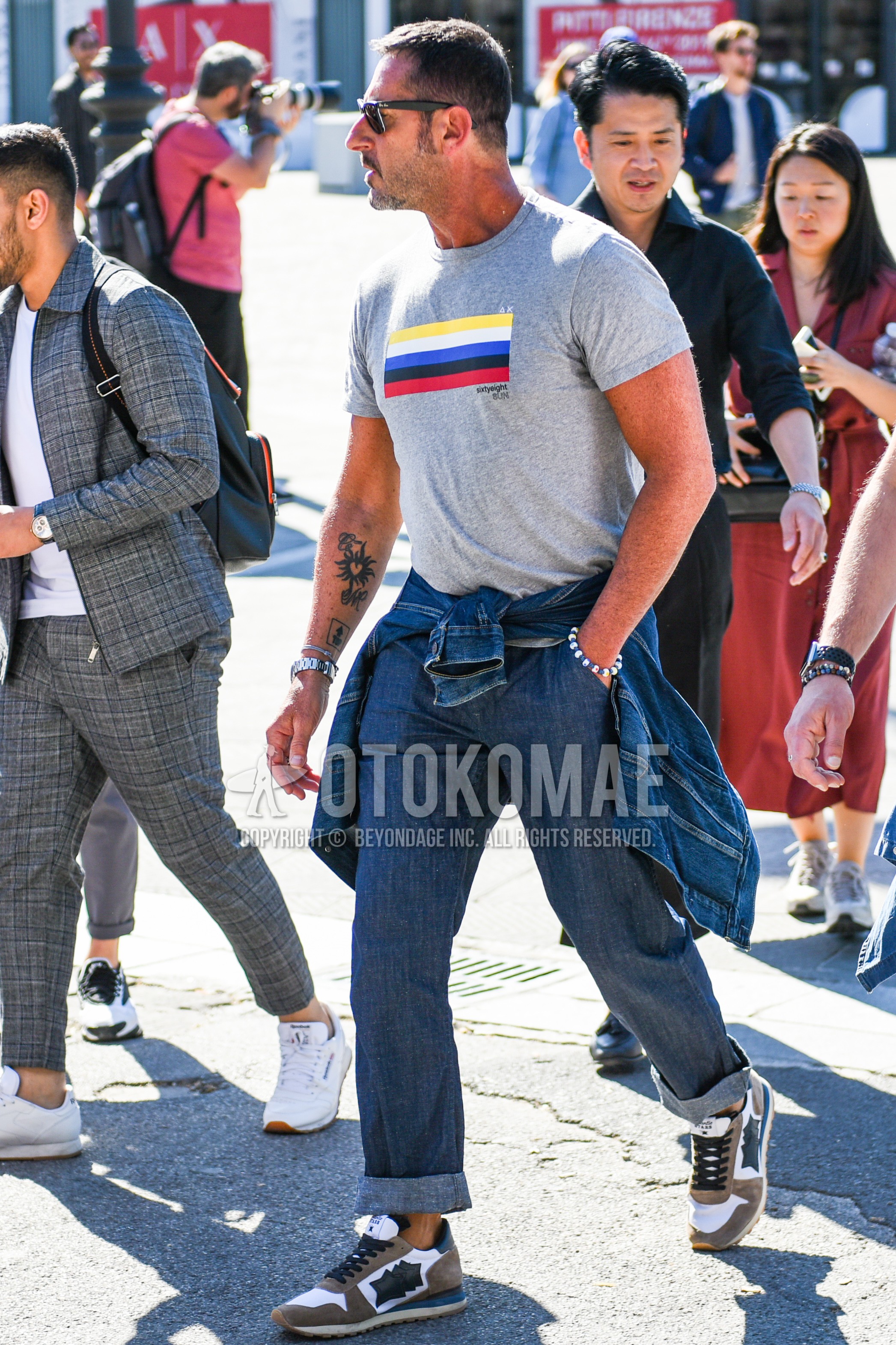 Men's summer outfit with black plain sunglasses, gray plain t-shirt, navy plain denim/jeans, white brown low-cut sneakers.