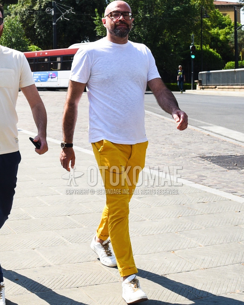 Men's spring summer outfit with brown tortoiseshell glasses, white plain t-shirt, yellow plain cotton pants, white low-cut sneakers.