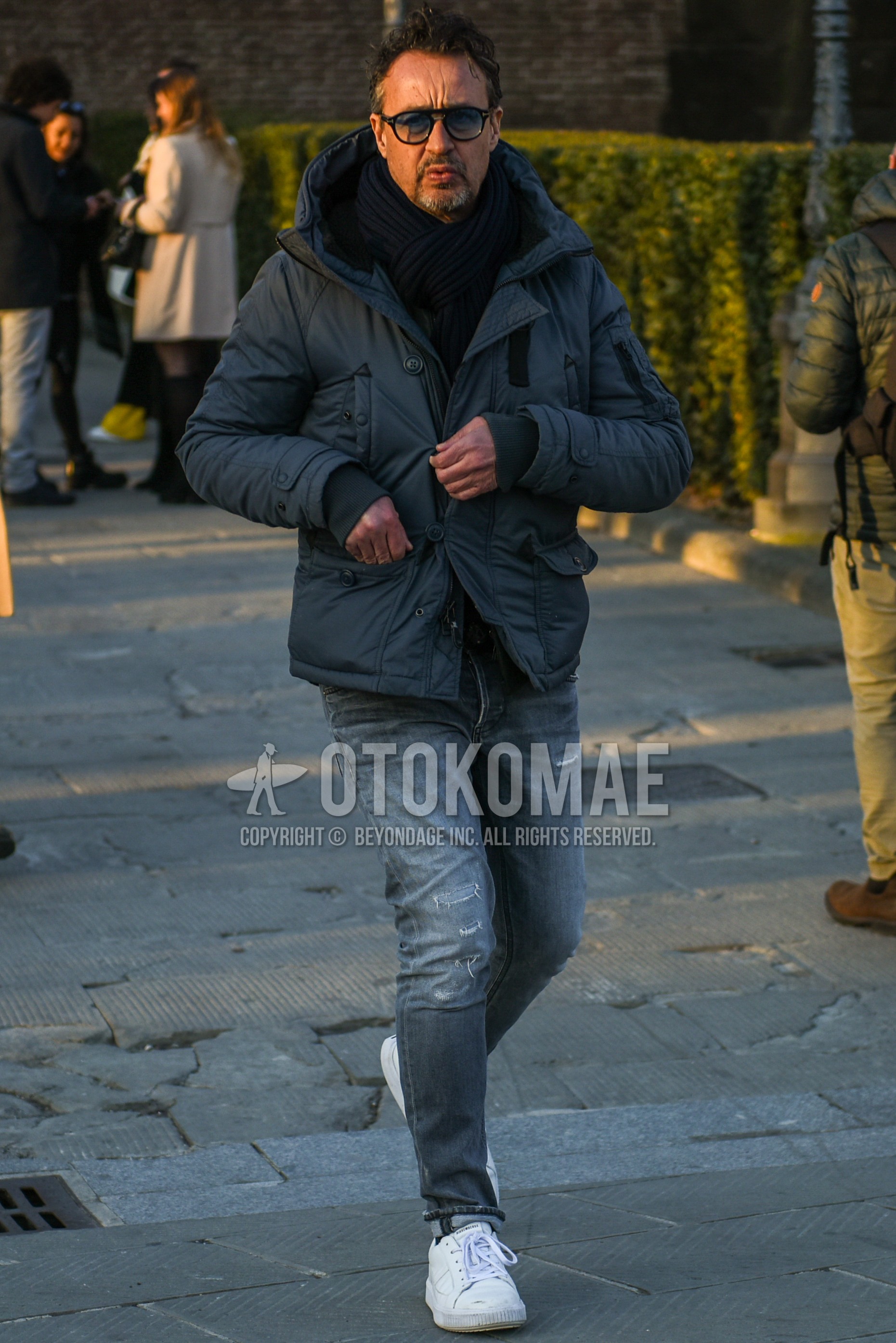 Men's winter outfit with black plain sunglasses, black plain scarf, gray plain down jacket, gray plain damaged jeans, white low-cut sneakers.