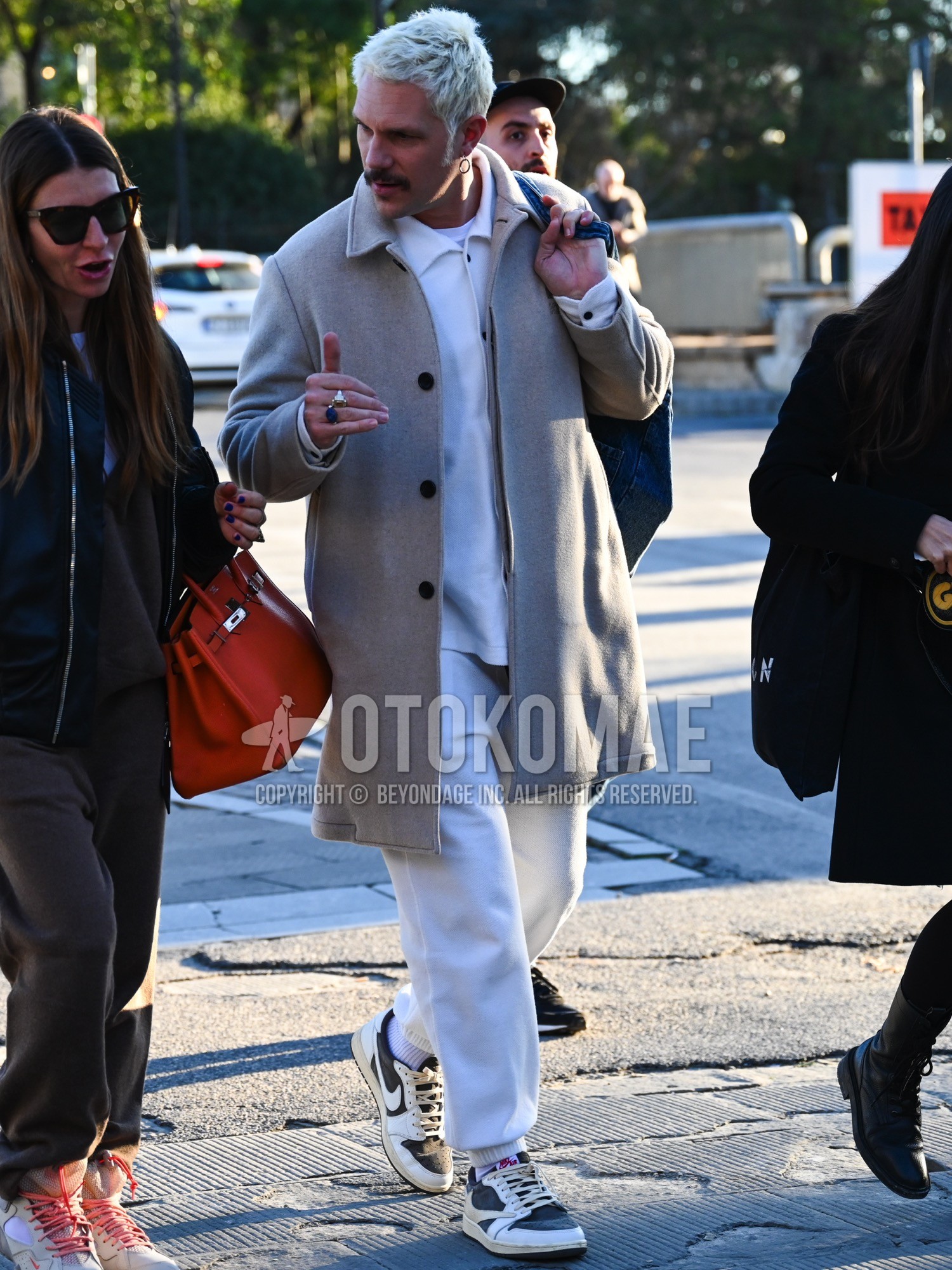 Men's autumn winter outfit with beige plain stenkarrer coat, white plain shirt, black plain t-shirt, white plain sweatpants, white plain socks, navy low-cut sneakers, navy plain tote bag.