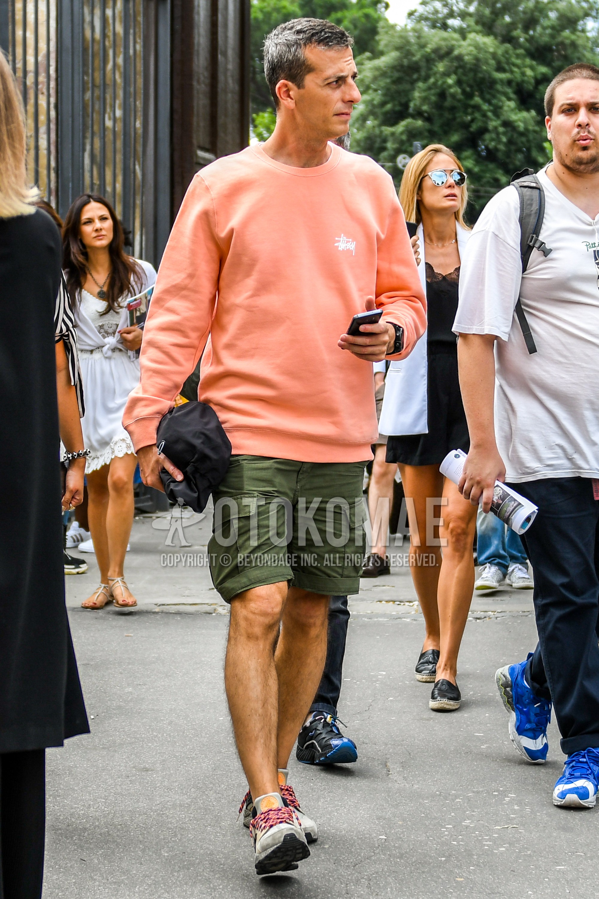 Men's spring summer outfit with orange plain sweatshirt, olive green plain short pants, plain cargo pants, gray low-cut sneakers.