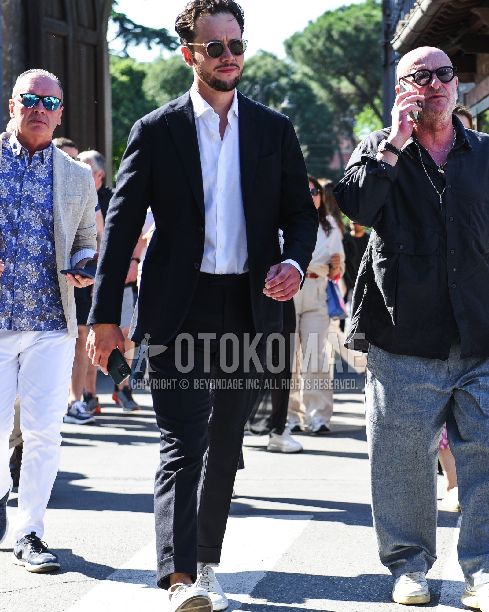 Men's spring summer outfit with clear plain sunglasses, white plain shirt, white low-cut sneakers, black plain suit.