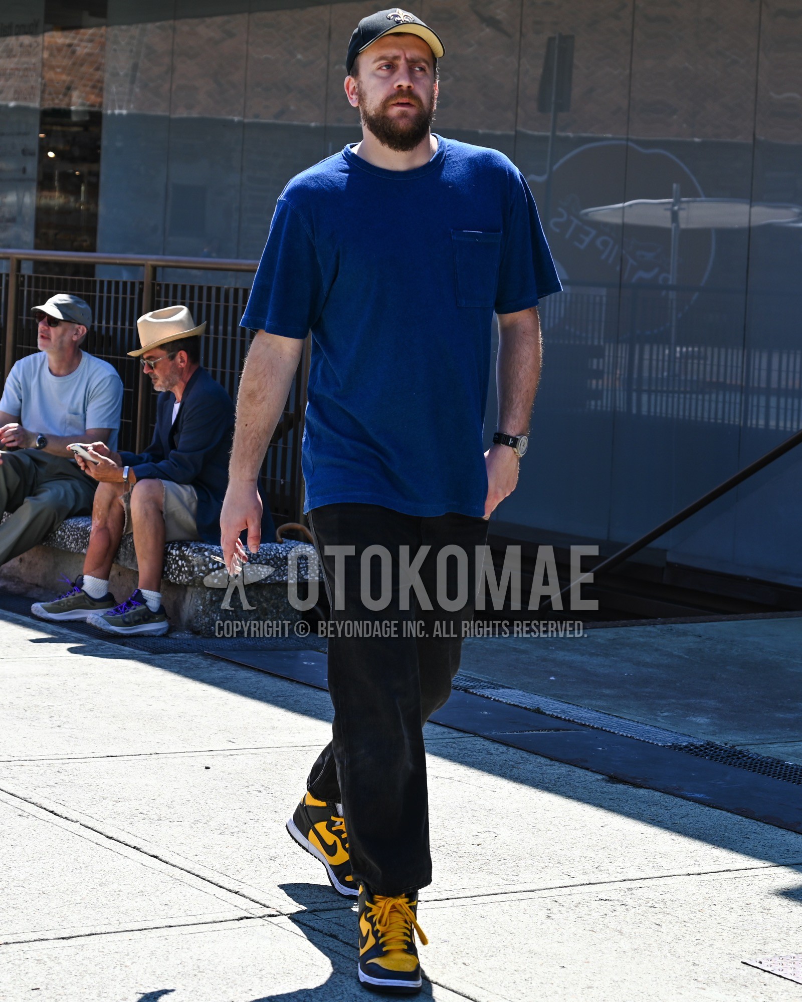 Men's spring summer outfit with black one point baseball cap, navy one point t-shirt, black plain chinos, yellow high-cut sneakers.