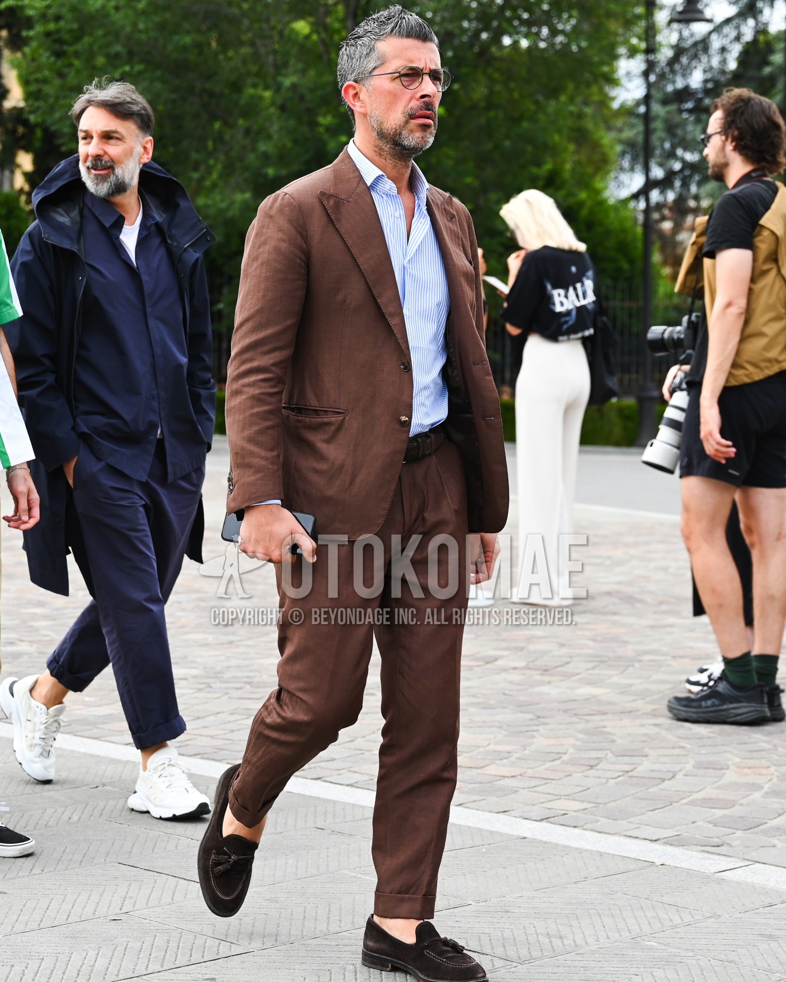 Men's spring summer autumn outfit with clear plain glasses, light blue stripes shirt, brown tassel loafers leather shoes, brown plain suit.