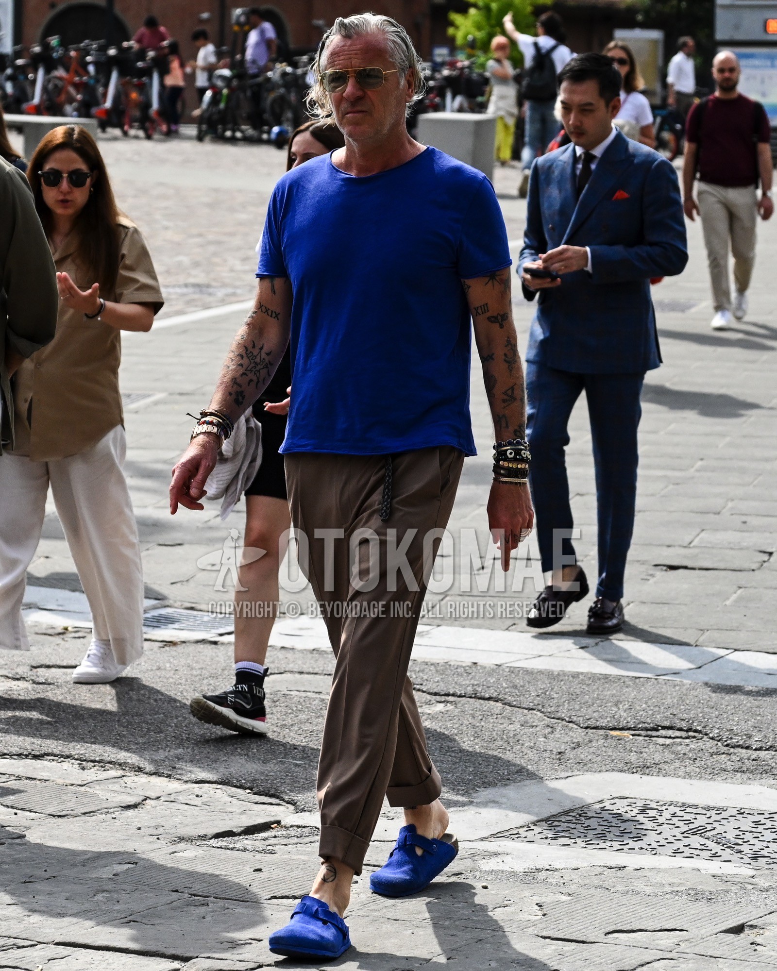 Men's spring summer outfit with blue plain sunglasses, blue plain t-shirt, brown plain chinos, blue leather sandals.