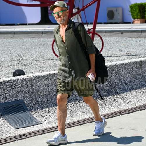 ニューエラのグリーンレタードのベースボールキャップ、グリーン無地のメガネ、オリーブグリーン無地のシャツ、オリーブグリーン無地のショートパンツ、オリーブグリーン無地のカーゴパンツ、白ローカットのスニーカー、黒無地のバックパックを合わせた夏春のメンズコーデ・着こなし。