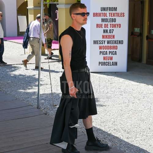 黒無地のサングラス、黒無地のアウター、黒無地のタンクトップ、ノースリーブの黒無地のTシャツ、黒無地のレザーベルト、黒無地のショートパンツ、黒無地のソックス、黒ローファーの革靴を合わせた夏春のメンズコーデ・着こなし。