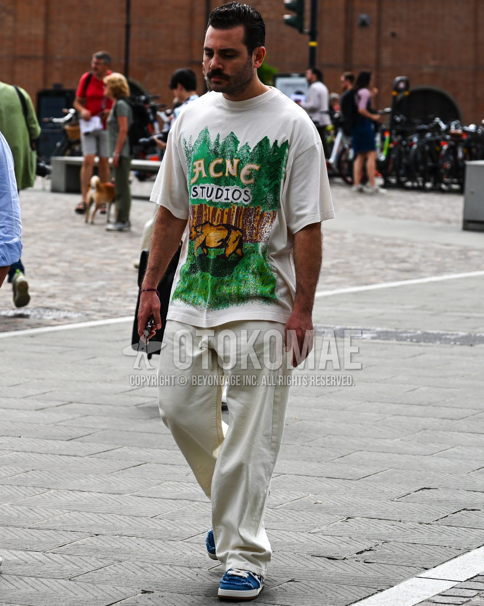 Men's spring summer outfit with white graphic t-shirt, white plain wide pants, blue low-cut sneakers.