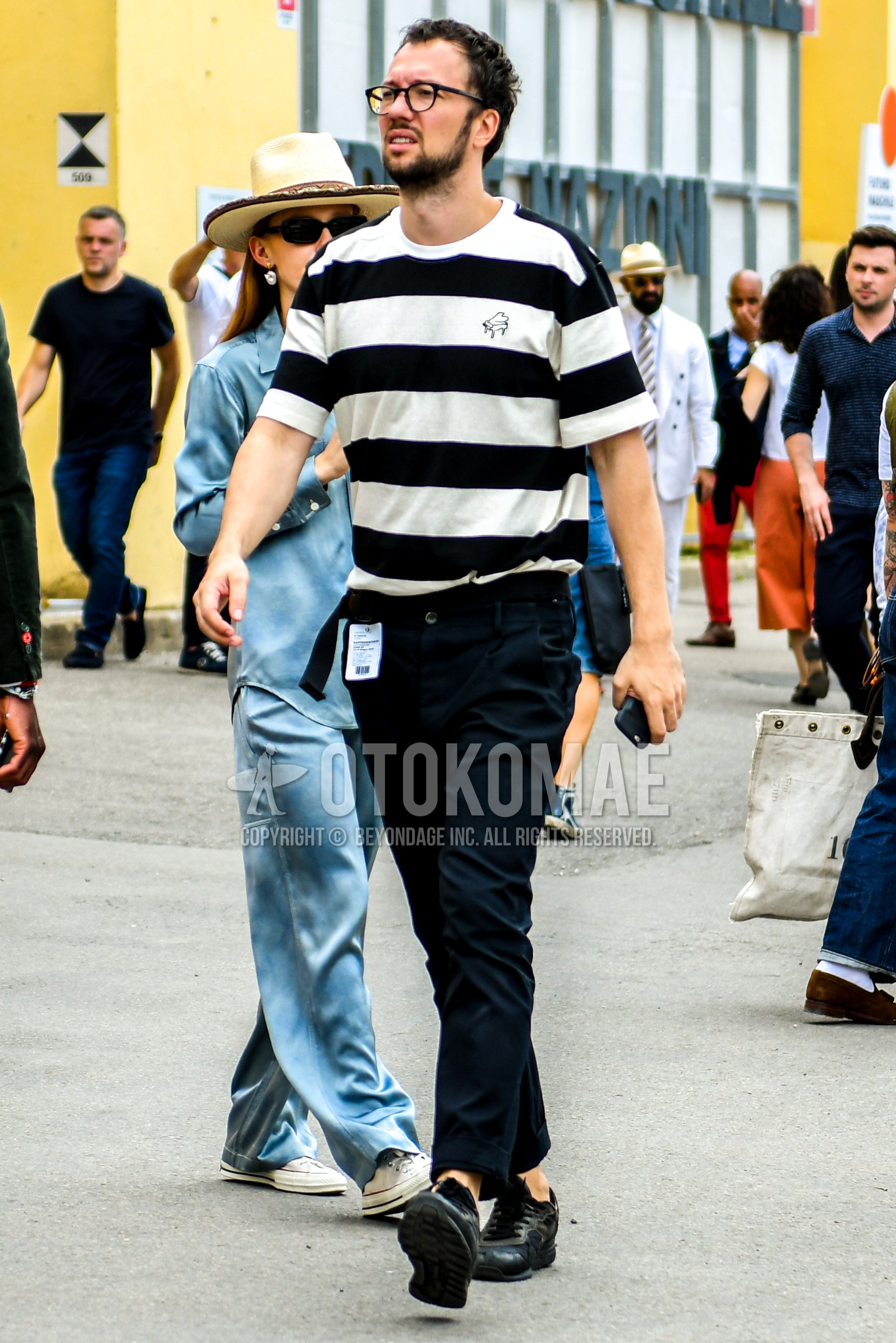 Men's summer outfit with plain glasses, white black horizontal stripes t-shirt, black plain ankle pants, black low-cut sneakers.