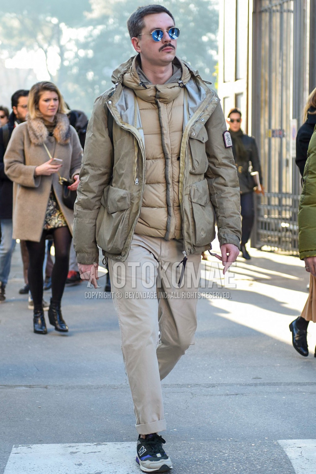 Men's winter outfit with gold plain sunglasses, beige plain field jacket/hunting jacket, beige plain inner down, beige plain chinos, gray low-cut sneakers.