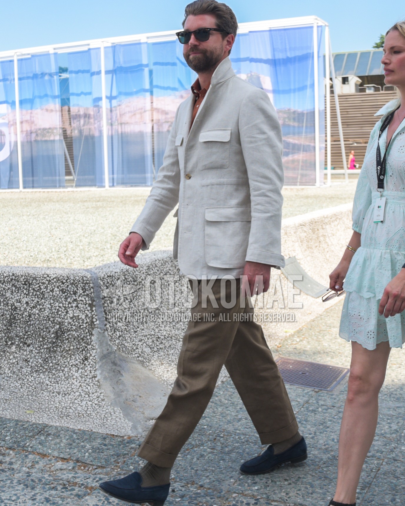 Men's spring summer autumn outfit with brown tortoiseshell sunglasses, white plain tailored jacket, brown plain shirt, brown plain slacks, olive green plain socks, navy suede shoes leather shoes, navy  loafers leather shoes.
