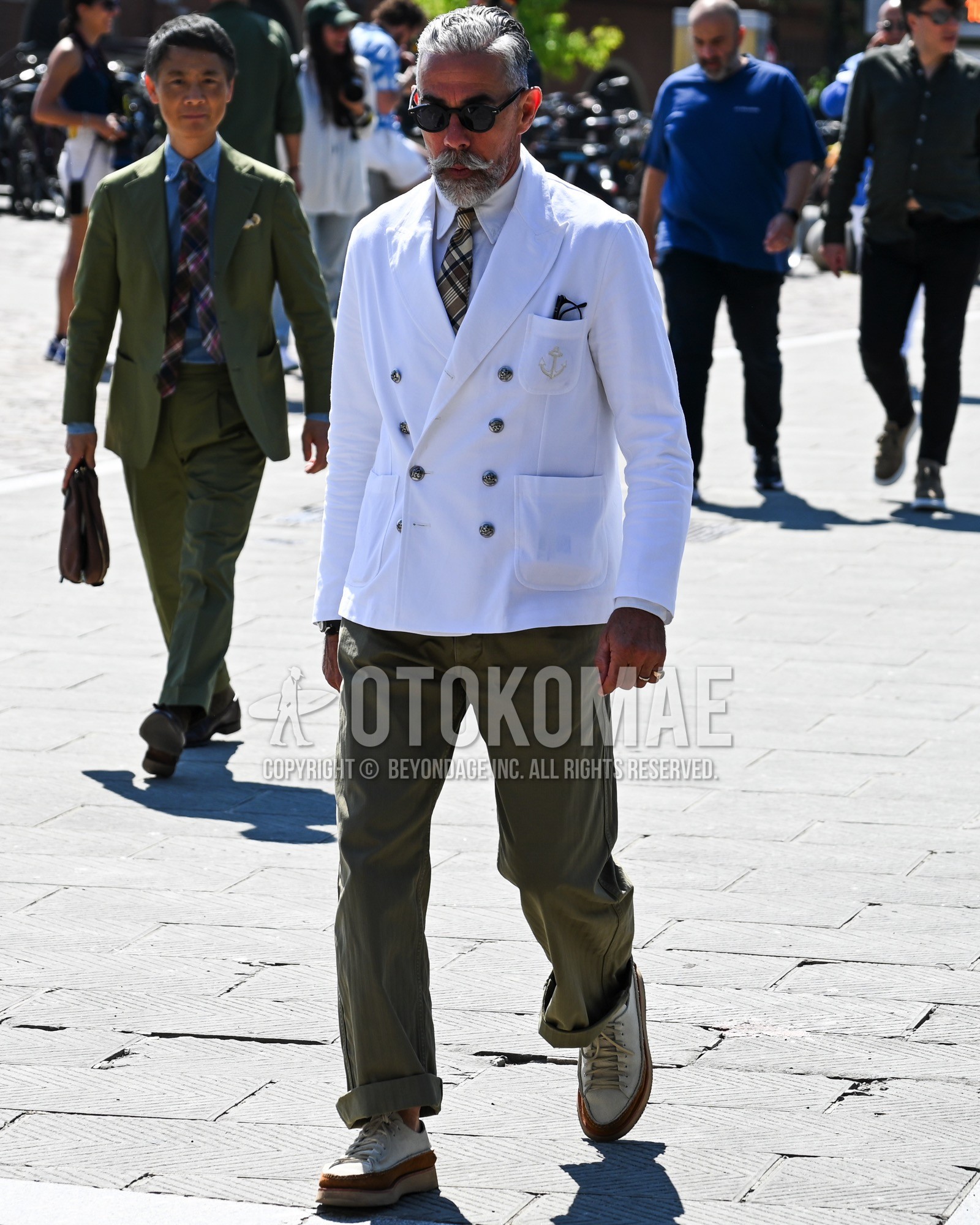 Men's spring summer autumn outfit with black plain sunglasses, white plain tailored jacket, white plain shirt, olive green plain chinos, white low-cut sneakers, white check necktie.
