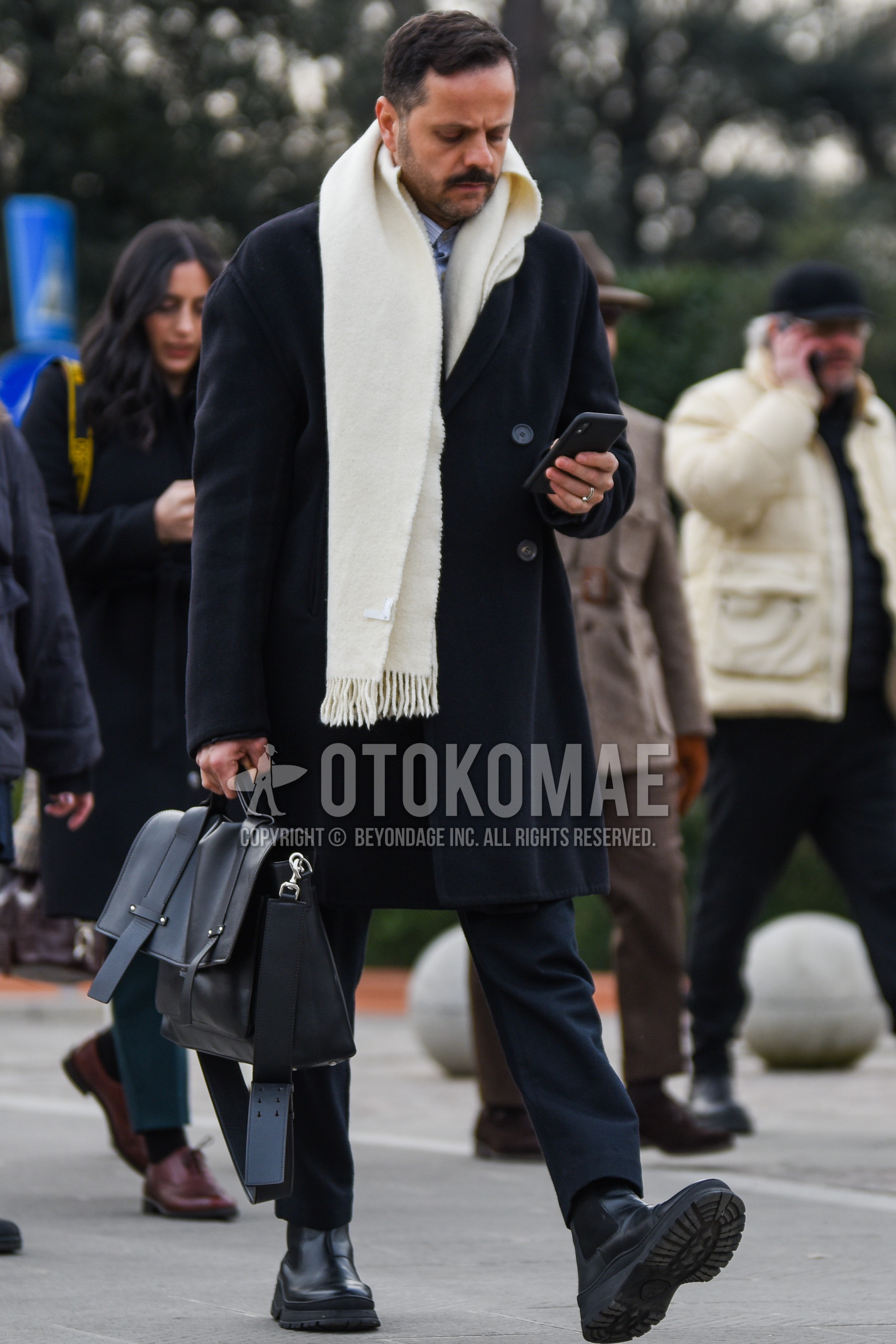 Men's autumn winter outfit with white plain scarf, black plain chester coat, dark gray plain slacks, black side-gore boots, black plain briefcase/handbag.