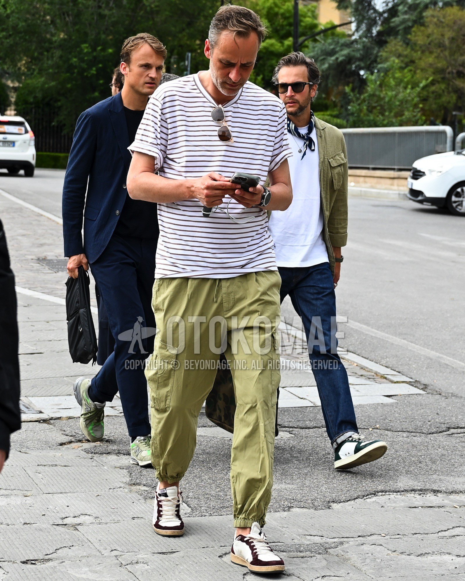 Men's spring summer outfit with white horizontal stripes t-shirt, beige plain cargo pants, white low-cut sneakers.