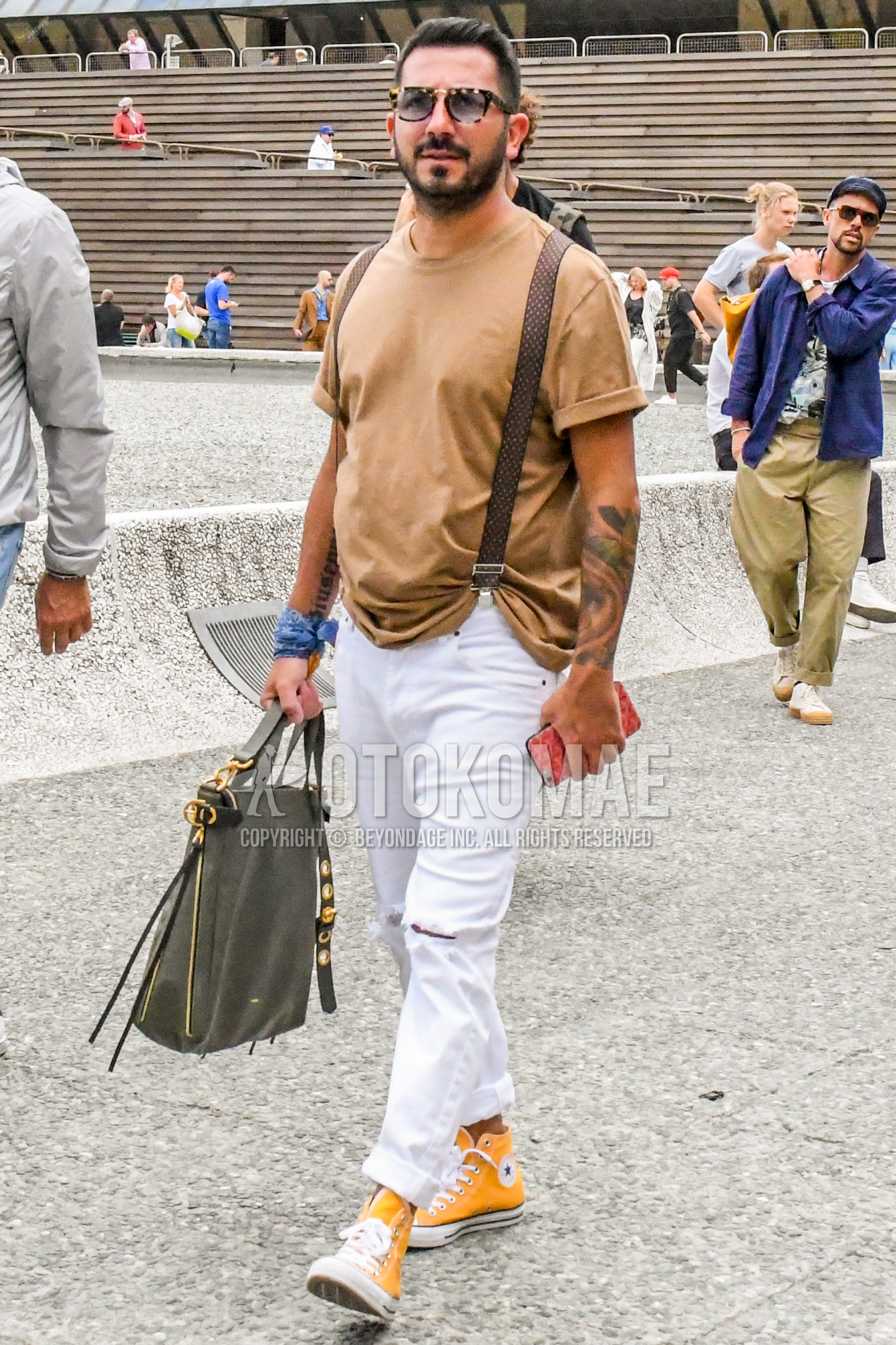Men's spring summer outfit with beige tortoiseshell sunglasses, beige plain t-shirt, brown belt suspenders, white plain damaged jeans, yellow high-cut sneakers, gray plain briefcase/handbag.