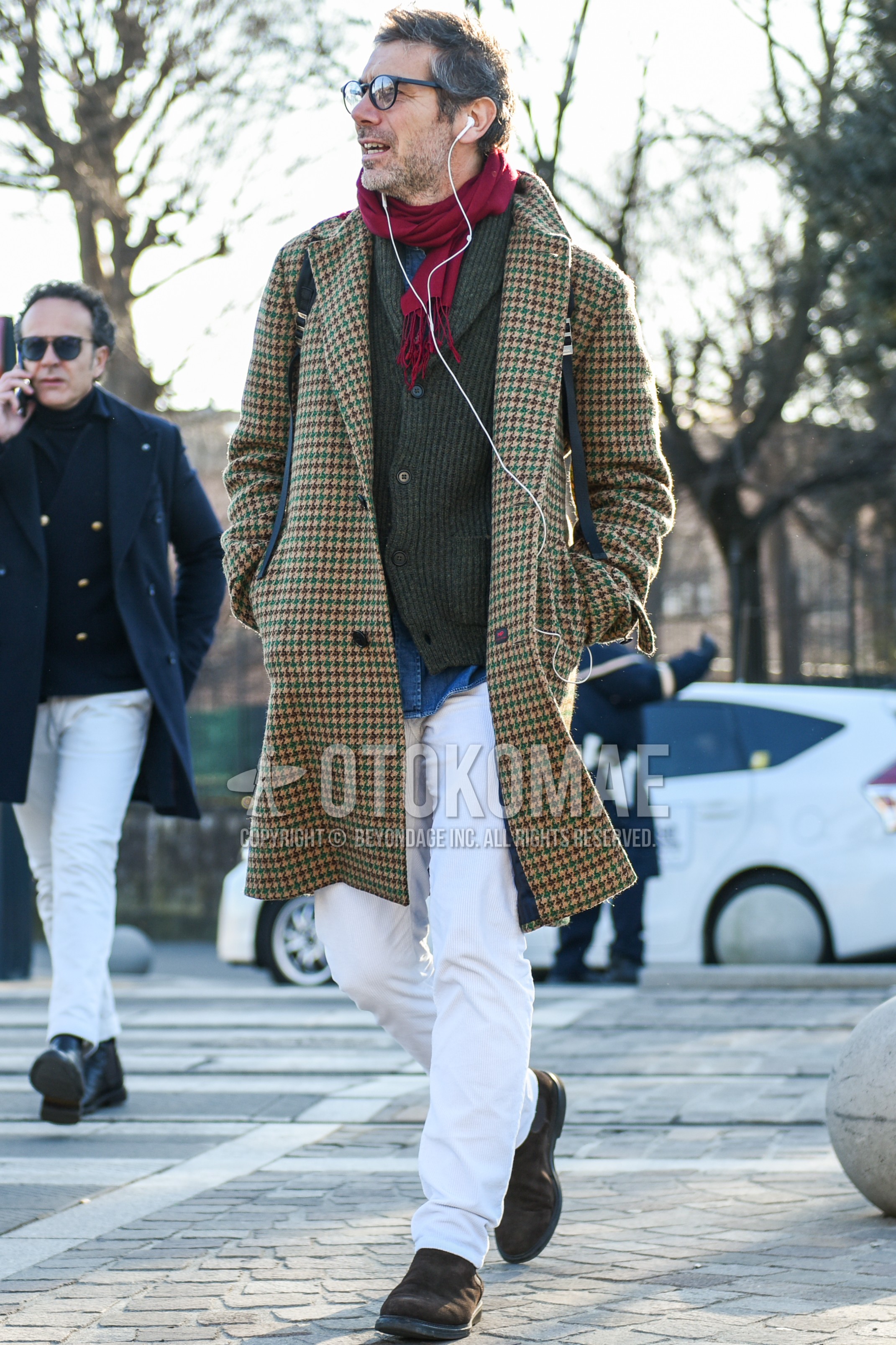 Men's autumn winter outfit with black plain glasses, red plain scarf, beige check chester coat, gray plain cardigan, white plain cotton pants, brown side-gore boots.