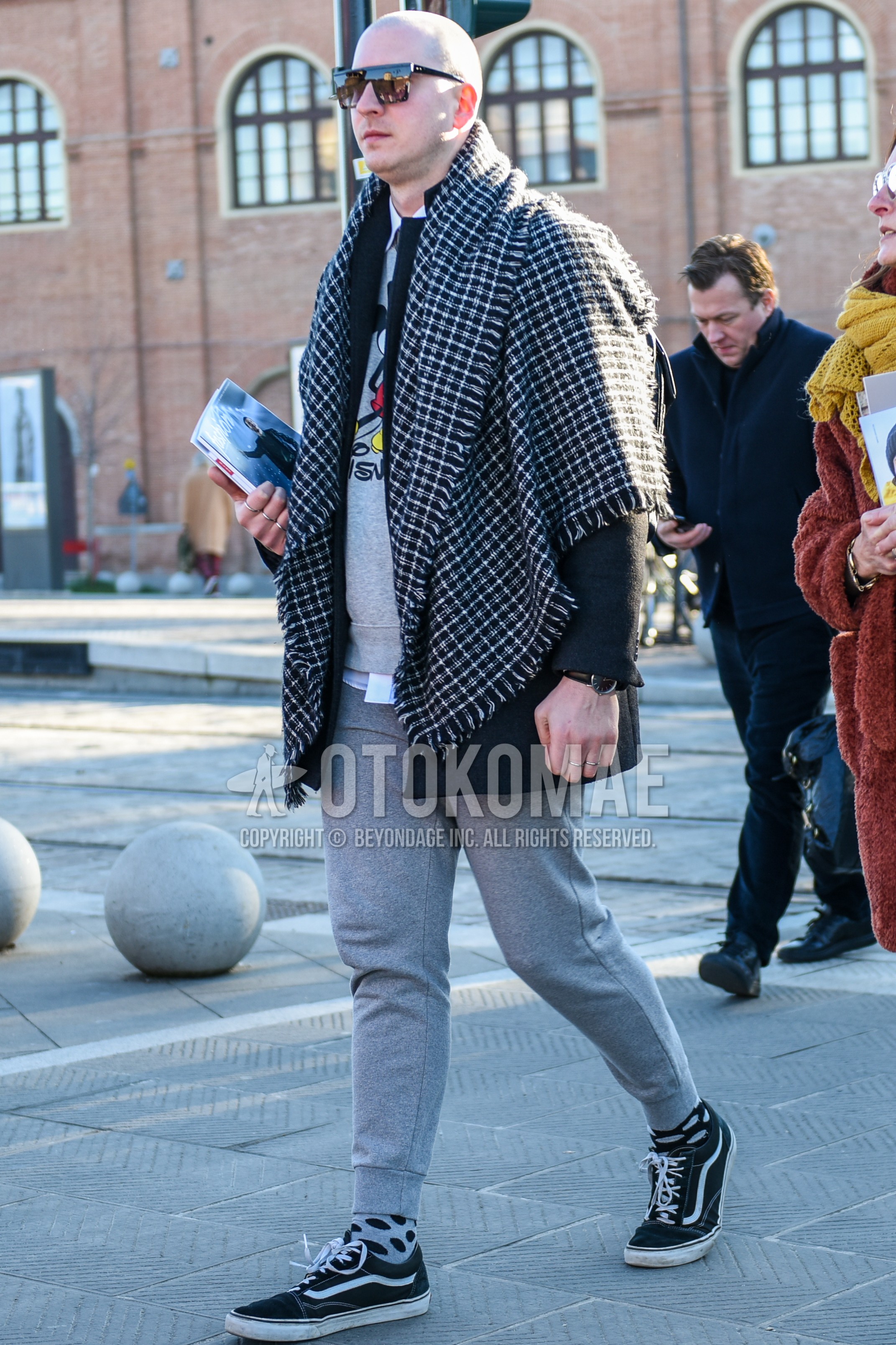 Men's autumn winter outfit with black plain sunglasses, black white check scarf, gray graphic sweatshirt, white plain shirt, gray plain sweatpants, gray dots socks, black low-cut sneakers.