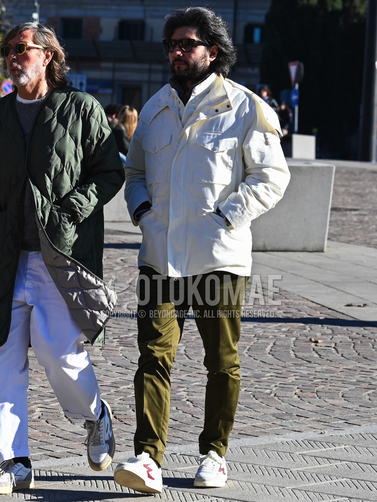 Men's autumn winter outfit with black plain sunglasses, brown check scarf, white plain military jacket, white plain shirt, olive green plain slacks, white low-cut sneakers.