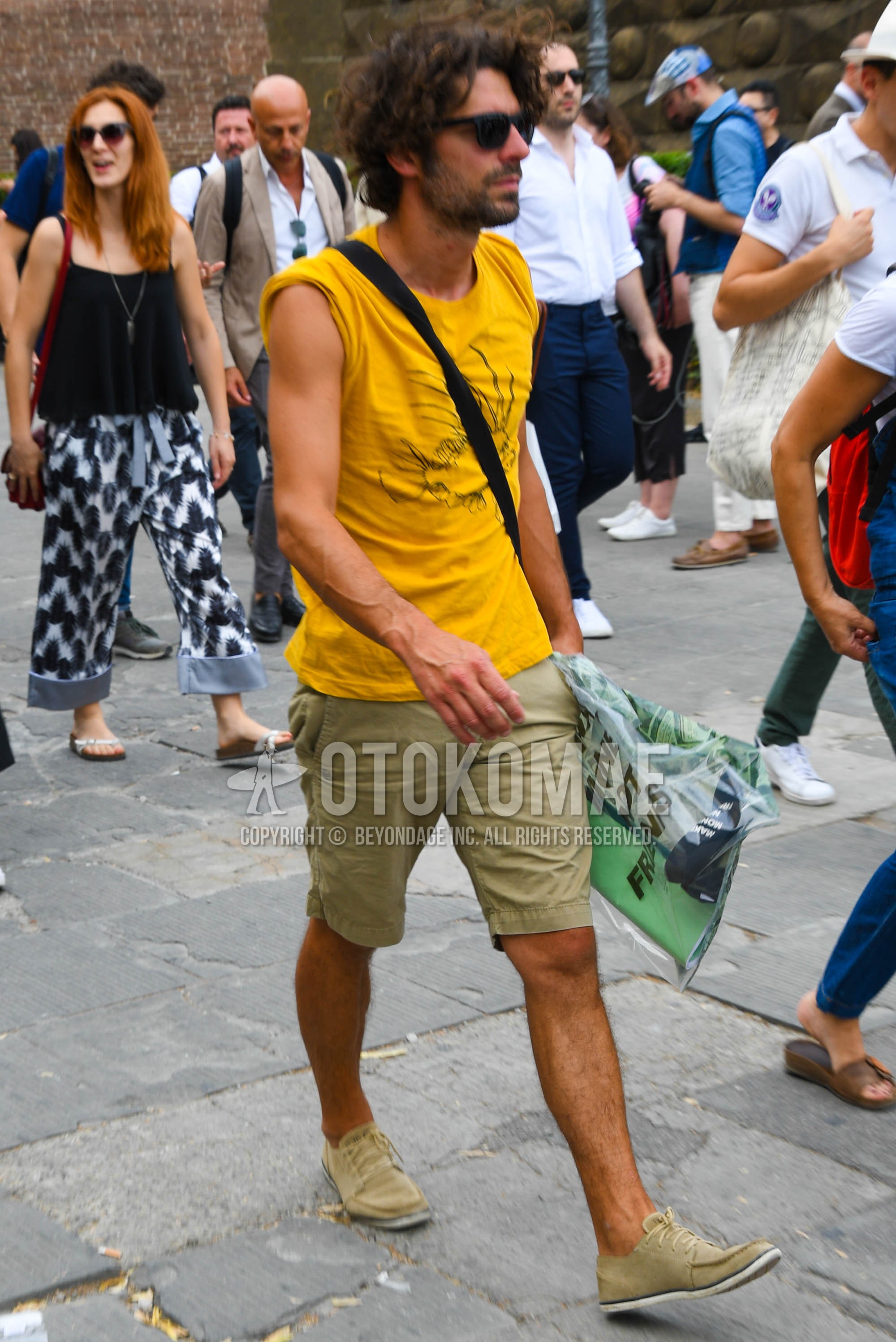 Men's summer outfit with plain sunglasses, yellow graphic t-shirt, beige plain short pants, beige low-cut sneakers.