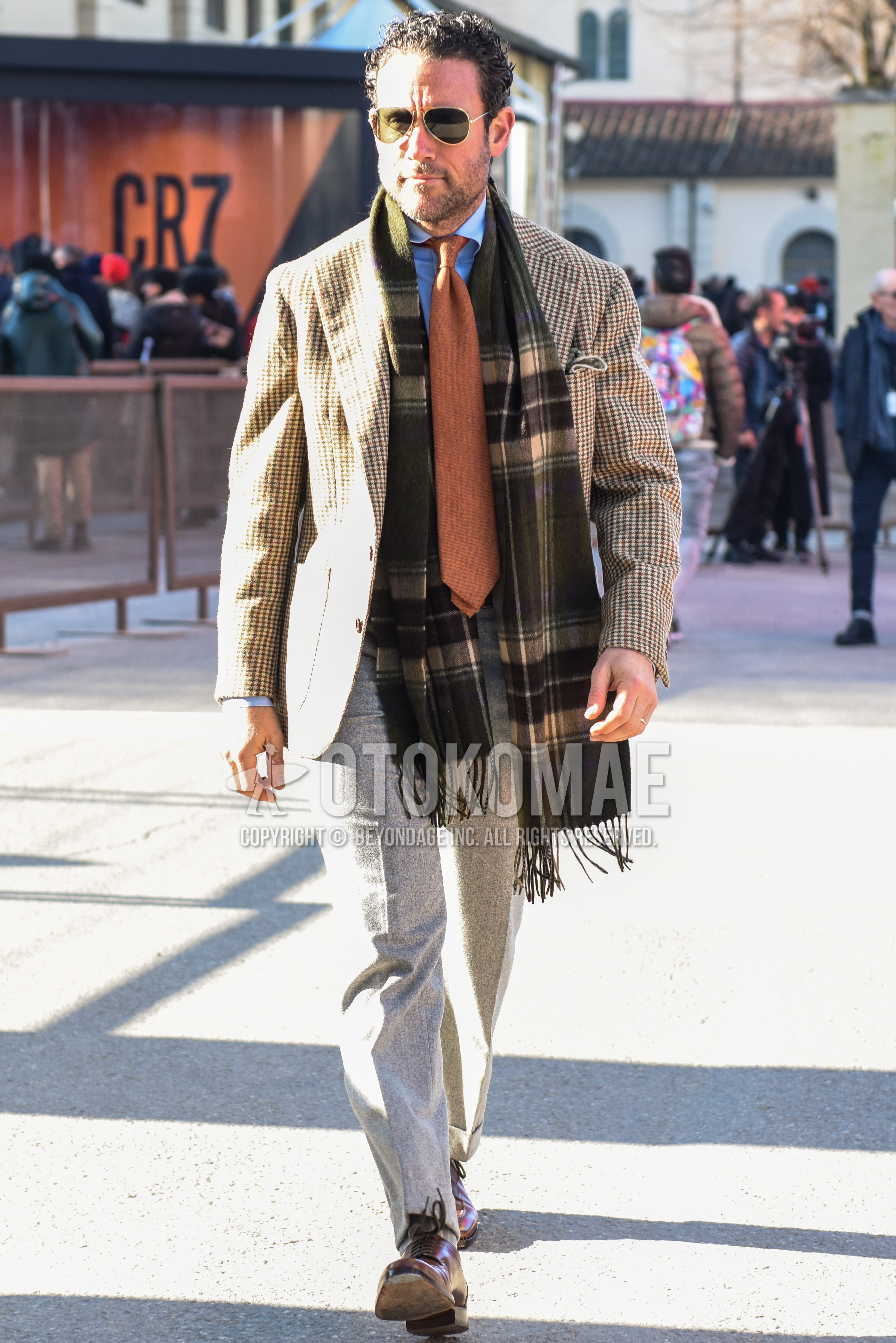 Men's autumn winter outfit with gold plain sunglasses, gray check scarf, beige check chester coat, light blue plain shirt, gray plain slacks, gray plain ankle pants, brown u-tip shoes leather shoes, orange plain necktie.