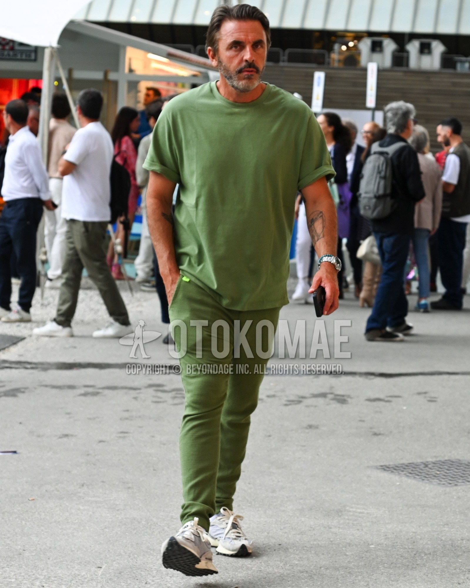 Men's spring summer outfit with green plain t-shirt, green plain chinos, white low-cut sneakers.