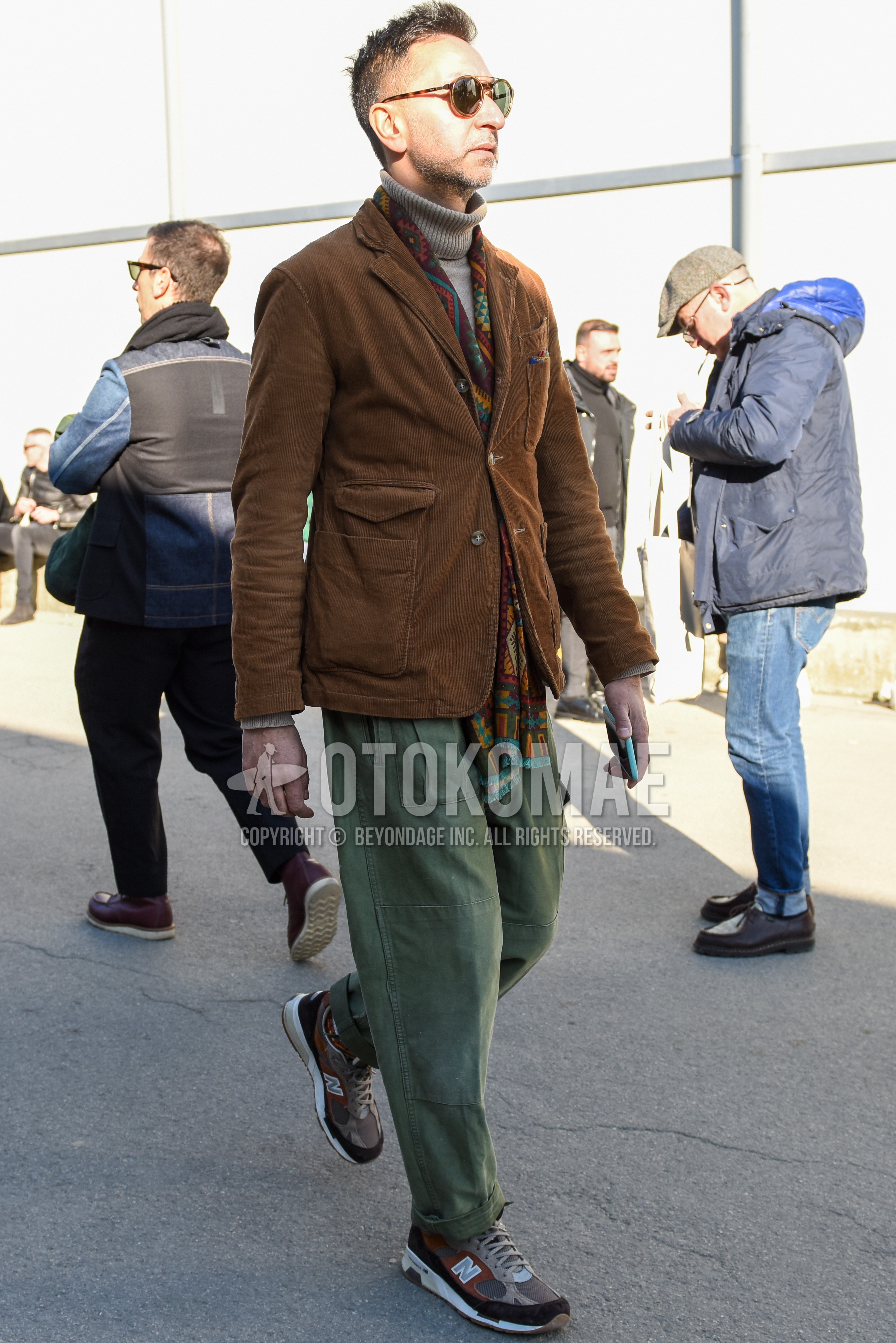 Men's spring autumn outfit with brown tortoiseshell sunglasses, brown scarf scarf, brown plain chester coat, beige plain turtleneck knit, olive green plain chinos, beige brown low-cut sneakers.