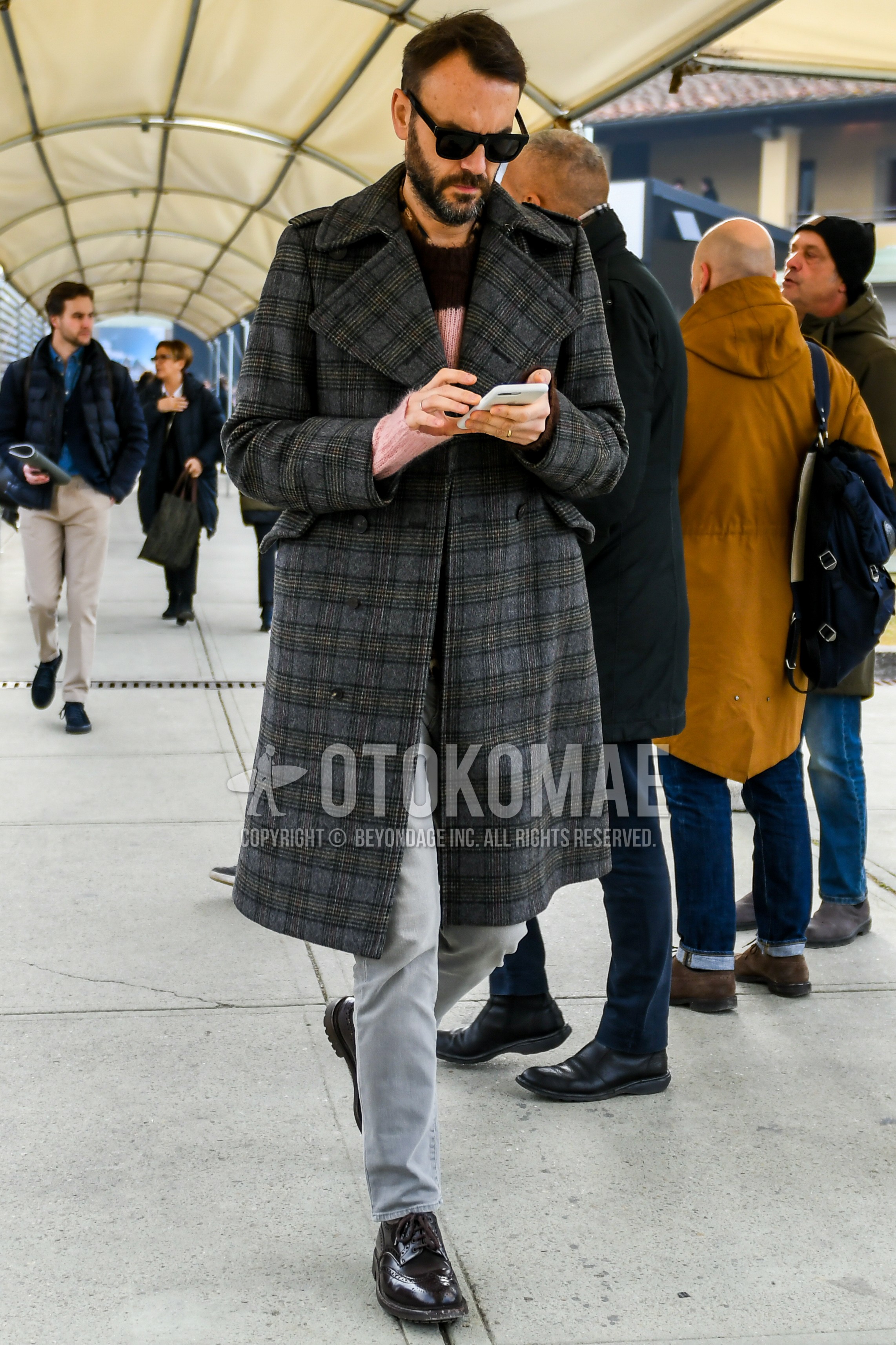 Men's winter outfit with black plain sunglasses, brown scarf scarf, dark gray check trench coat, pink brown tops/innerwear sweater, gray plain denim/jeans, brown wing-tip shoes leather shoes.