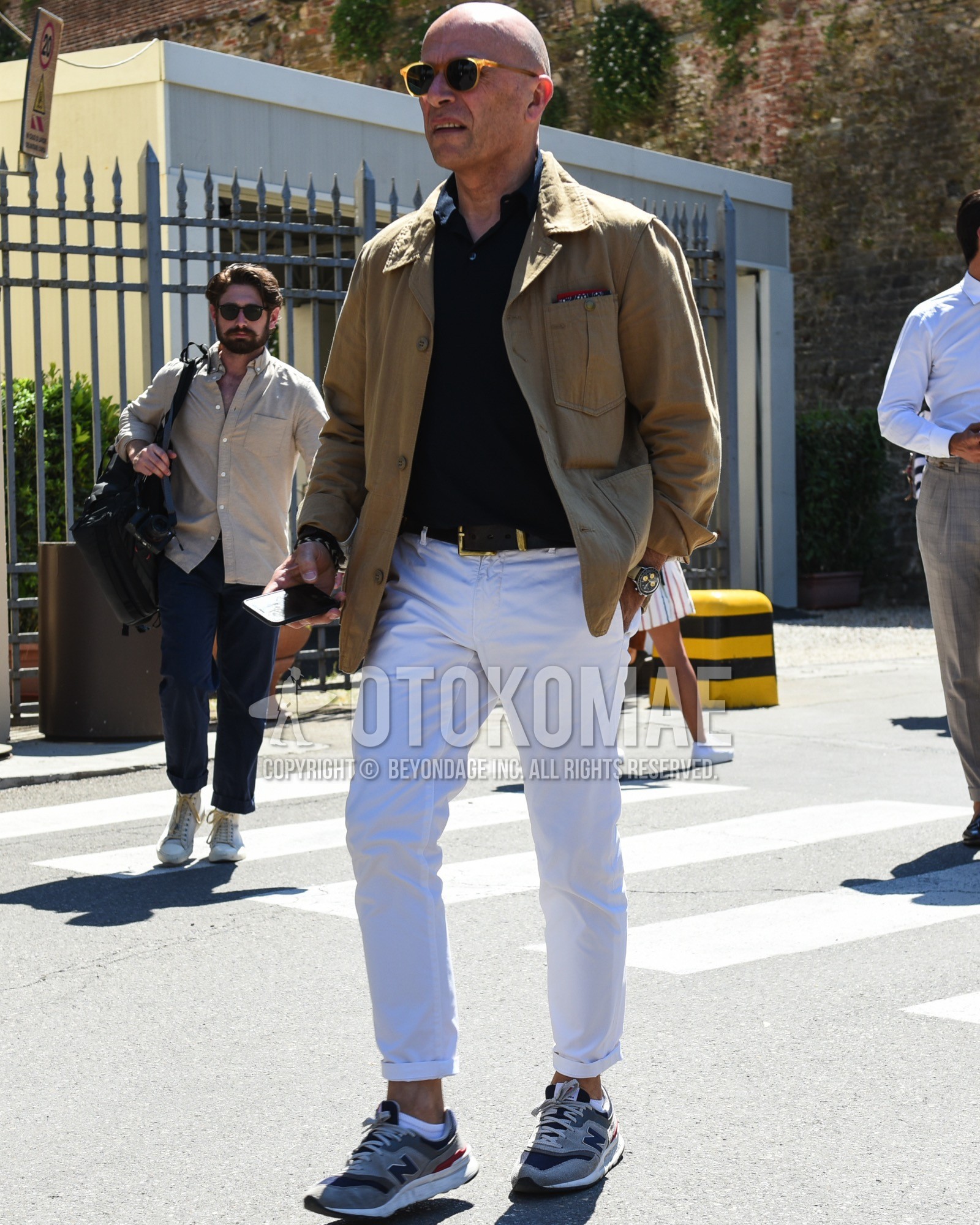 Men's spring summer outfit with brown plain sunglasses, beige plain tailored jacket, brown plain leather belt, white plain cotton pants, white plain socks, gray low-cut sneakers.