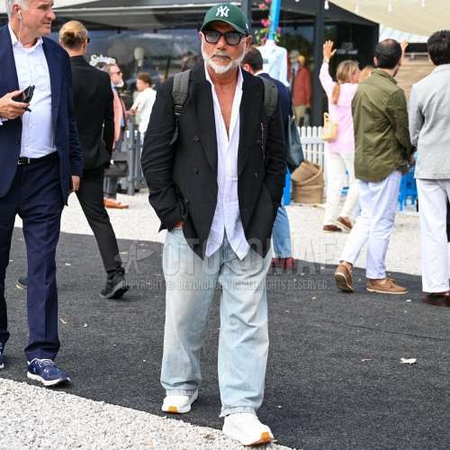 グリーンレタードのベースボールキャップ、ウェリントンの黒無地のサングラス、黒無地のテーラードジャケット、白無地のシャツ、ブルー無地のデニム/ジーンズ、白ローカットのスニーカー、グレー無地のバックパックを合わせた夏春のメンズコーデ・着こなし。