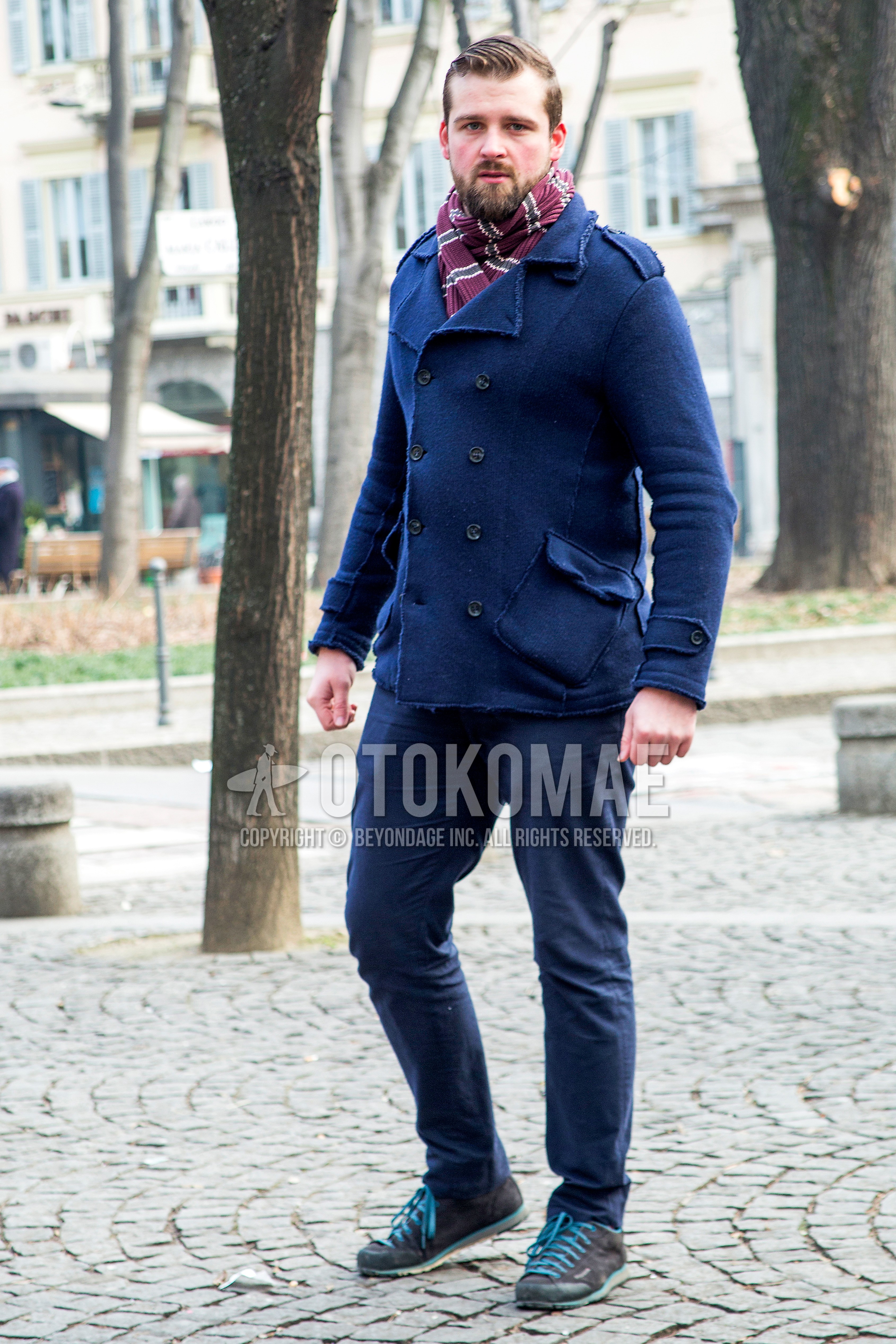 Men's winter outfit with red horizontal stripes scarf, navy plain p coat, navy plain chinos, gray low-cut sneakers.