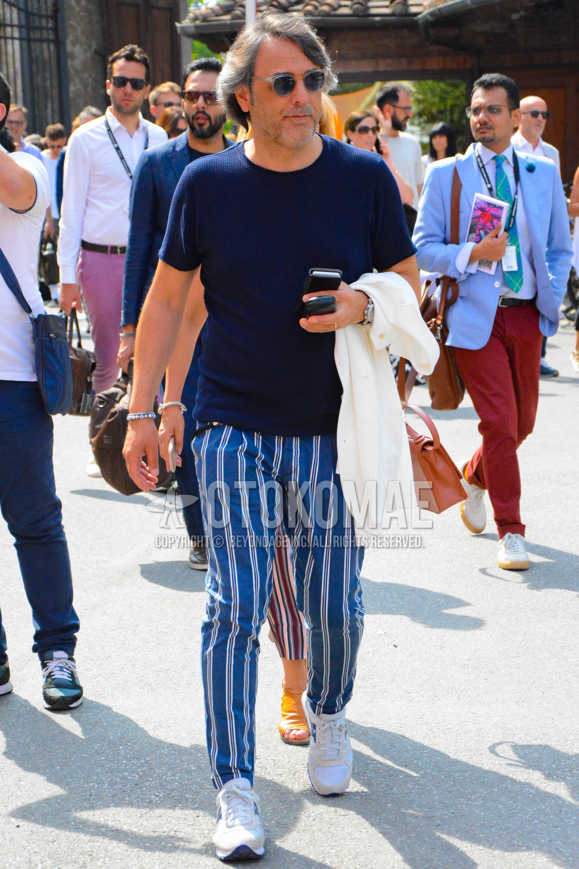 Men's spring summer outfit with clear plain sunglasses, navy plain t-shirt, blue stripes cotton pants, white low-cut sneakers.