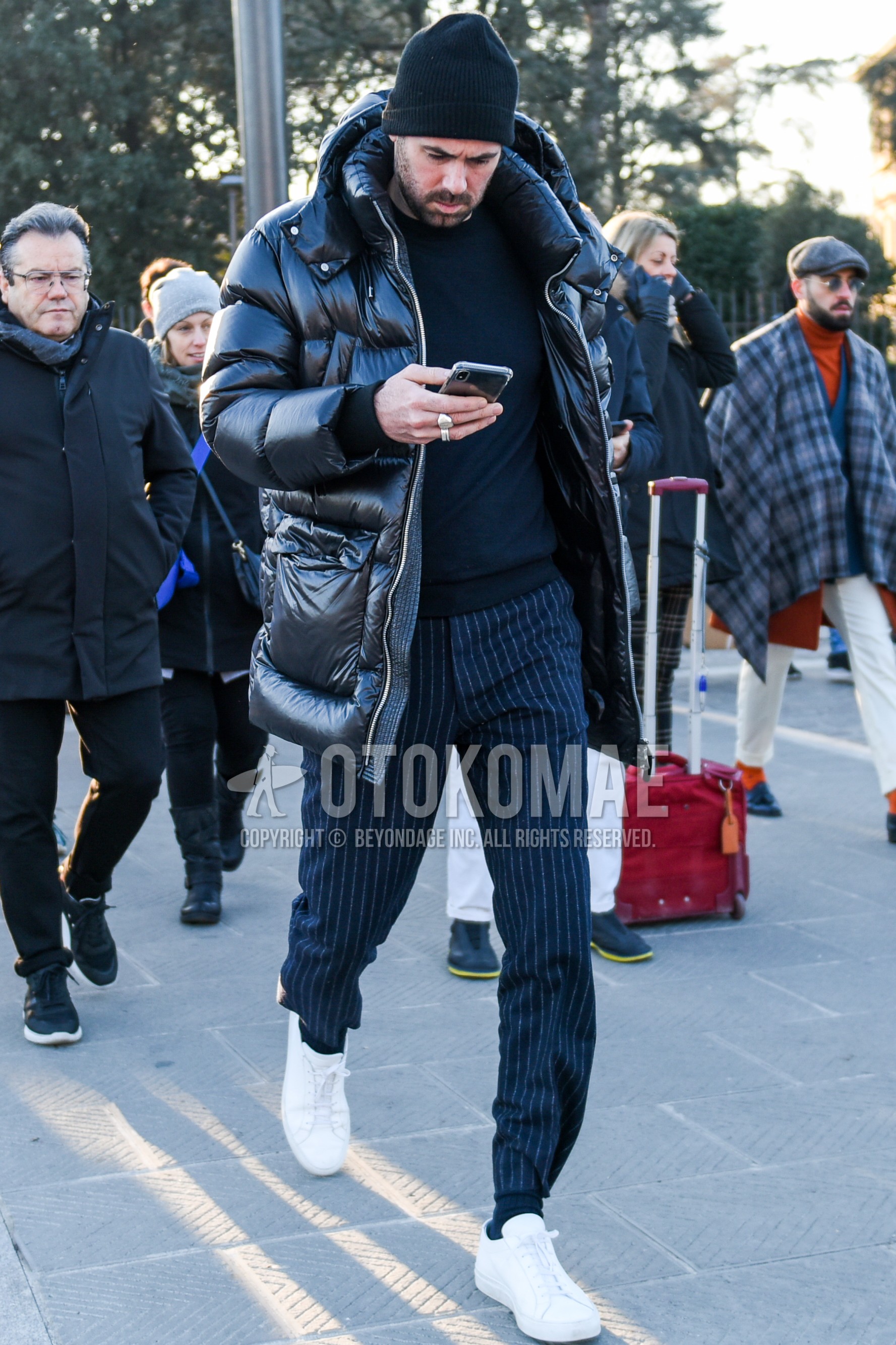 Men's winter outfit with black plain knit cap, black plain down jacket, black plain hooded coat, navy plain sweater, navy stripes slacks, white low-cut sneakers.