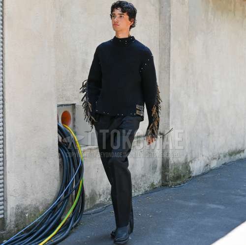 黒トップス/インナーのセーター、黒無地のスラックス、黒のブーツを合わせた夏春のメンズコーデ・着こなし。