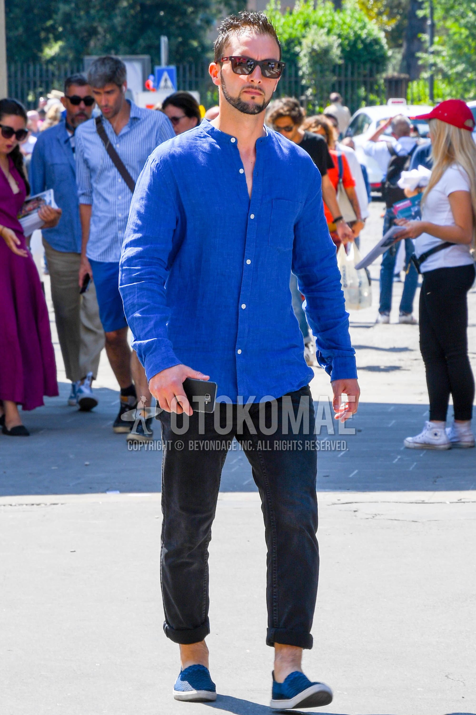 Men's spring summer autumn outfit with plain sunglasses, blue plain shirt, dark gray plain denim/jeans, blue slip-on sneakers.