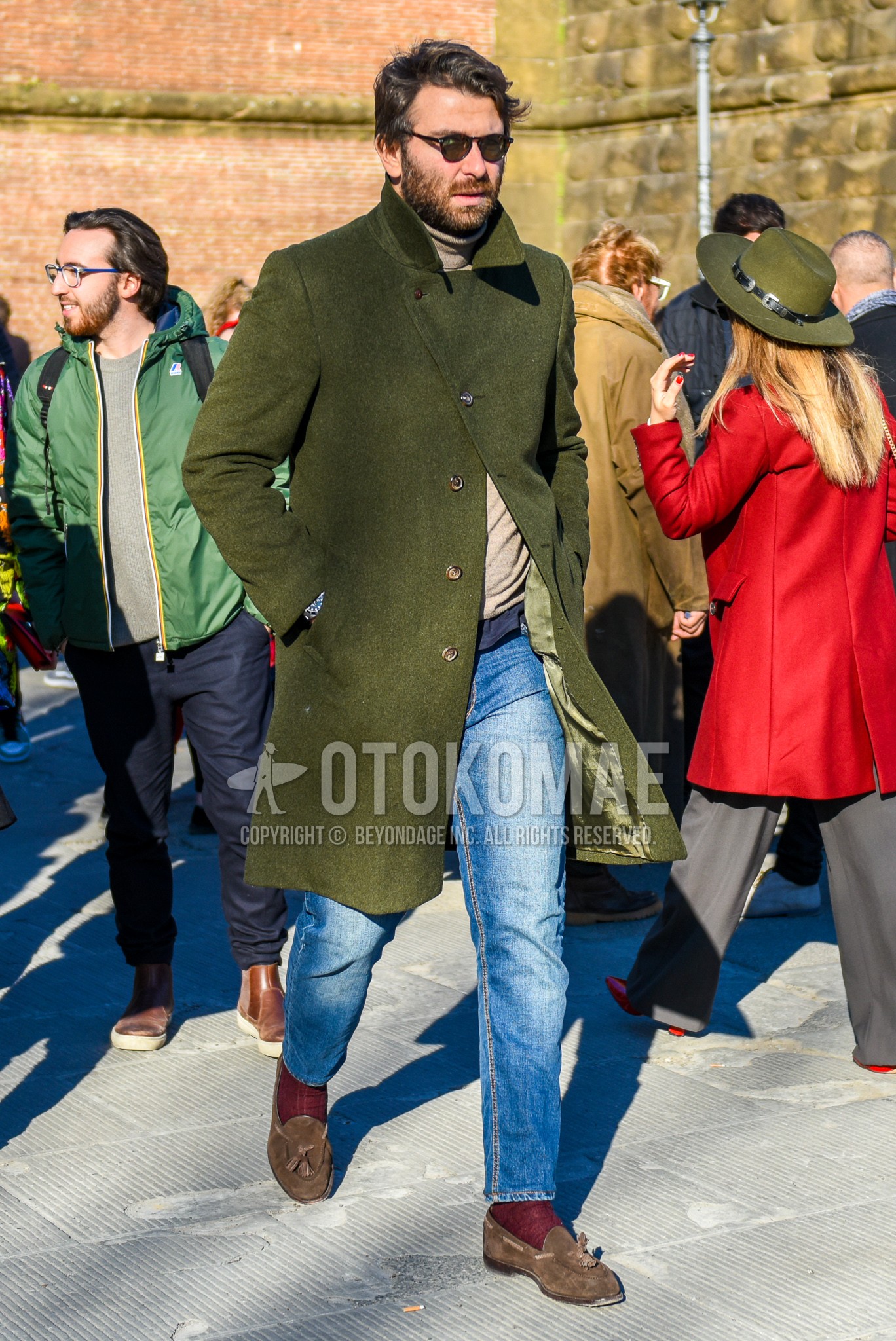 Men's autumn winter outfit with brown tortoiseshell sunglasses, olive green plain outerwear, beige plain turtleneck knit, blue plain denim/jeans, red plain socks, brown tassel loafers leather shoes.