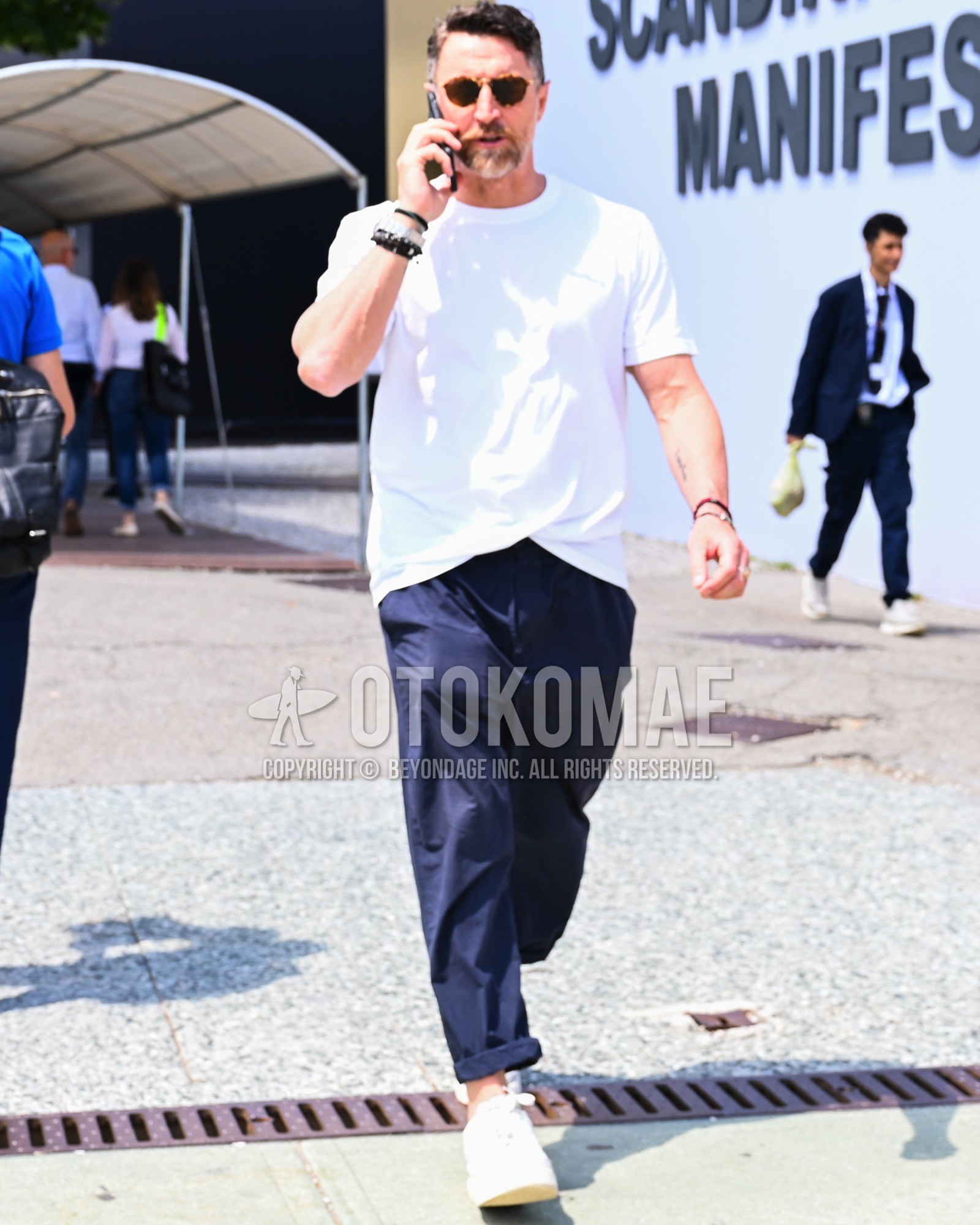 Men's spring summer outfit with black plain sunglasses, white plain t-shirt, navy plain chinos, white low-cut sneakers.