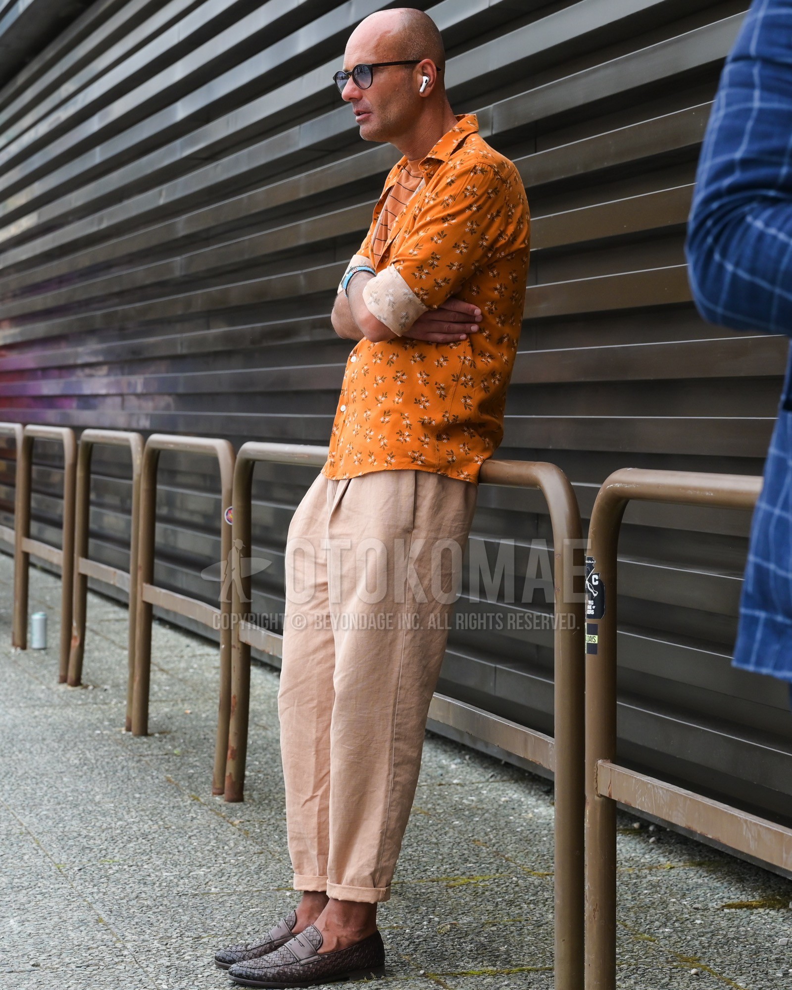 Men's spring summer autumn outfit with black plain sunglasses, orange whole  pattern shirt, beige plain chinos, brown coin loafers leather shoes.