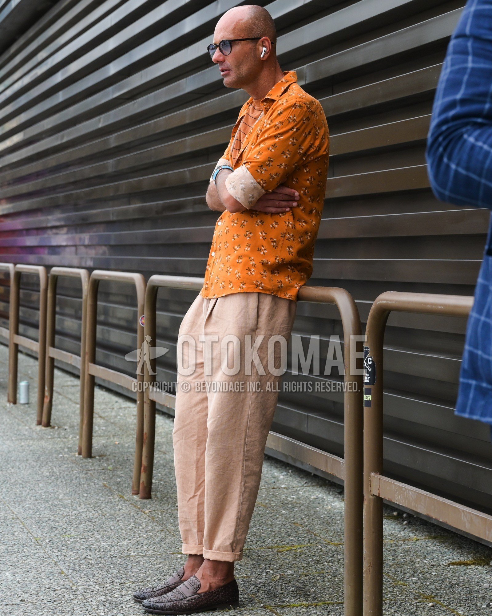 Men's spring summer autumn outfit with black plain sunglasses, orange whole pattern shirt, beige plain chinos, brown coin loafers leather shoes.