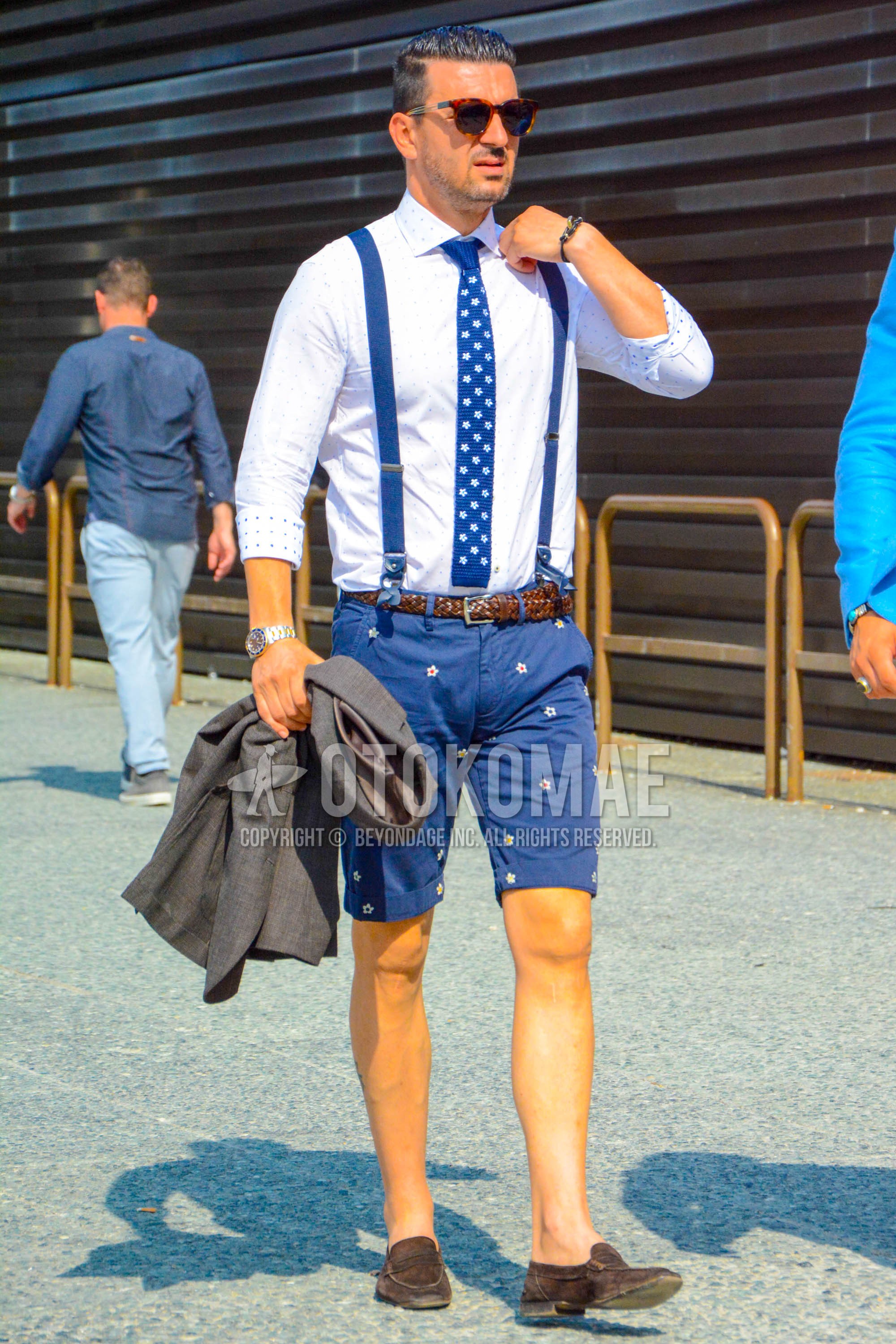 Men's spring summer outfit with brown tortoiseshell sunglasses, white dots shirt, blue plain suspenders, brown plain braided belt, brown plain leather belt, navy bottoms short pants, brown coin loafers leather shoes, blue necktie knit tie.