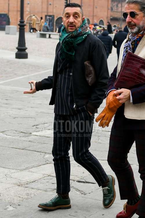 グリーンストールのマフラー/ストール、ダークグレー無地のアウター、ブラウン・ネイビーチェックのソックス、グリーンウィングチップの革靴、ブラウン無地のクラッチバッグ/セカンドバッグ/巾着、黒ストライプのスーツを合わせた秋冬のメンズコーデ・着こなし。