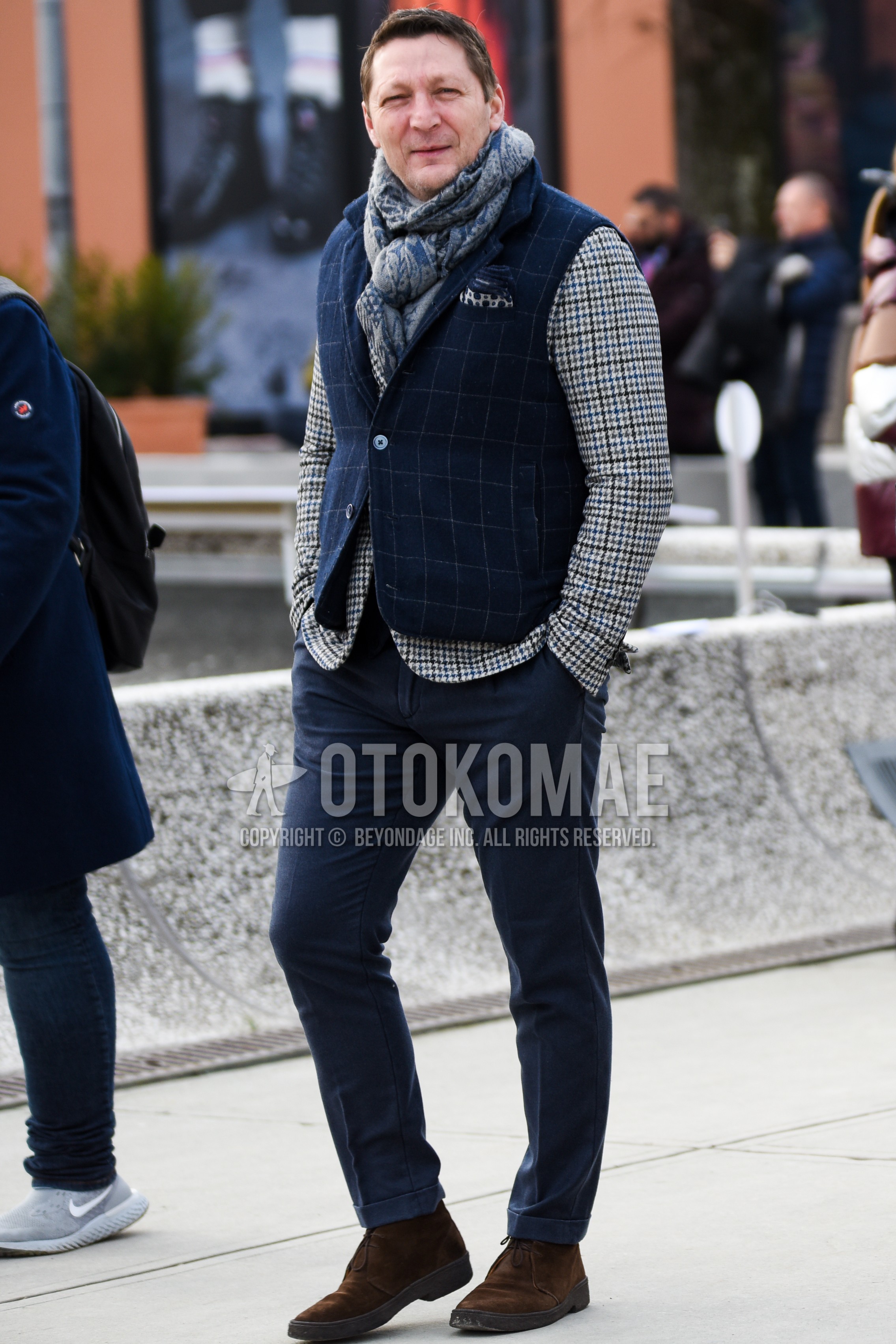 Men's autumn winter outfit with gray scarf scarf, navy check casual vest, gray check tailored jacket, navy plain chinos, brown chukka boots.
