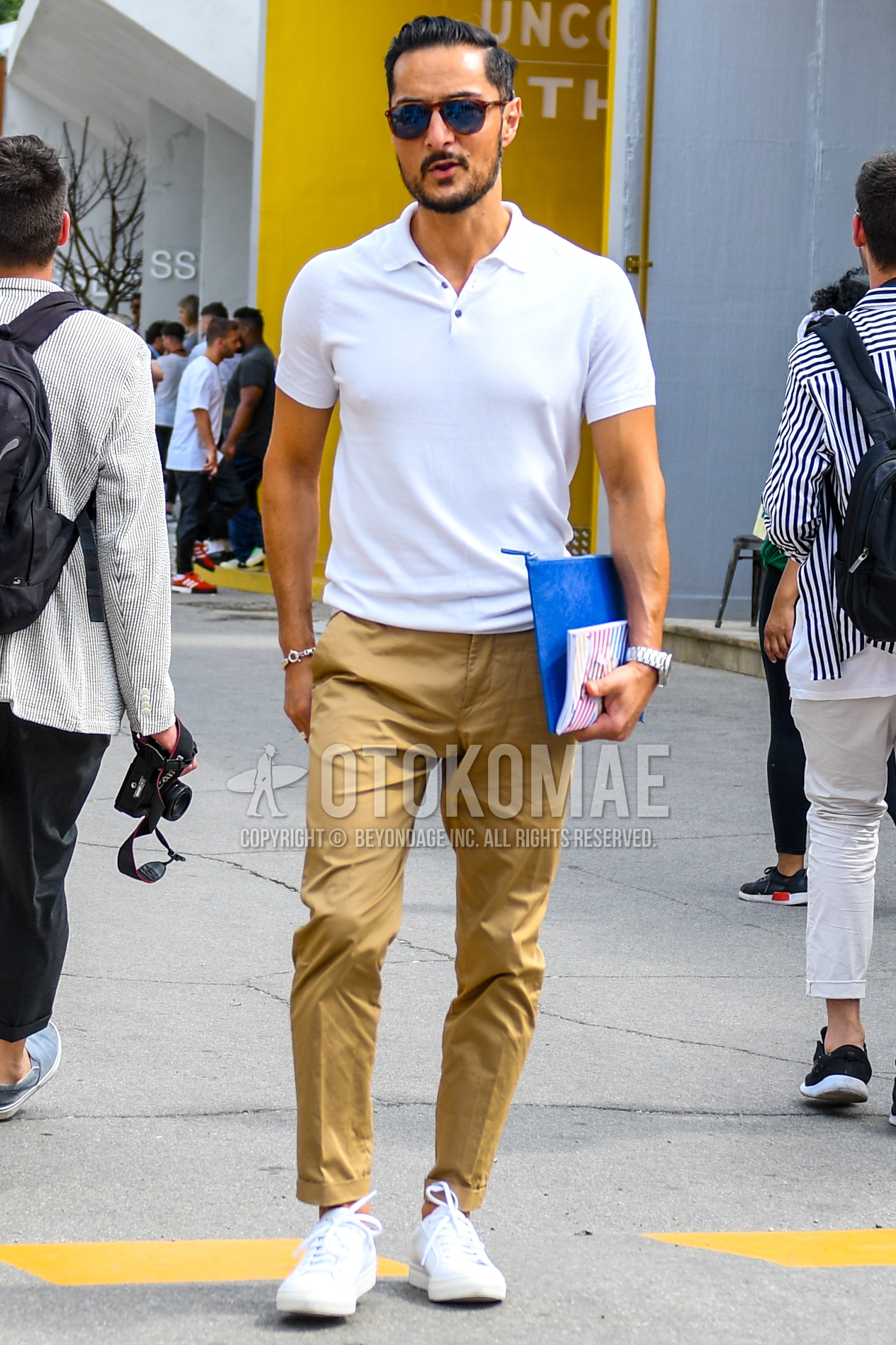 Men's spring summer outfit with brown tortoiseshell sunglasses, white plain polo shirt, beige plain chinos, white low-cut sneakers.