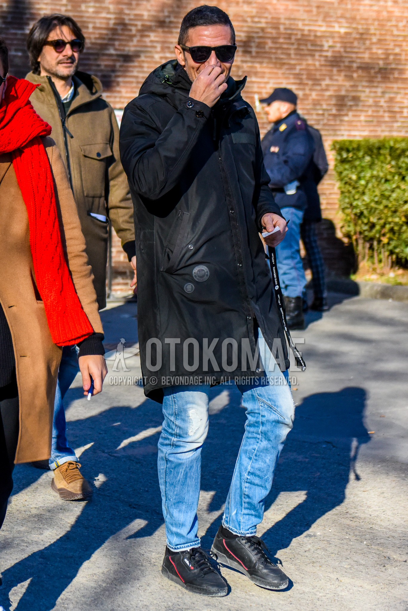 Men's winter outfit with plain sunglasses, black plain hooded coat, light blue plain denim/jeans, black low-cut sneakers.