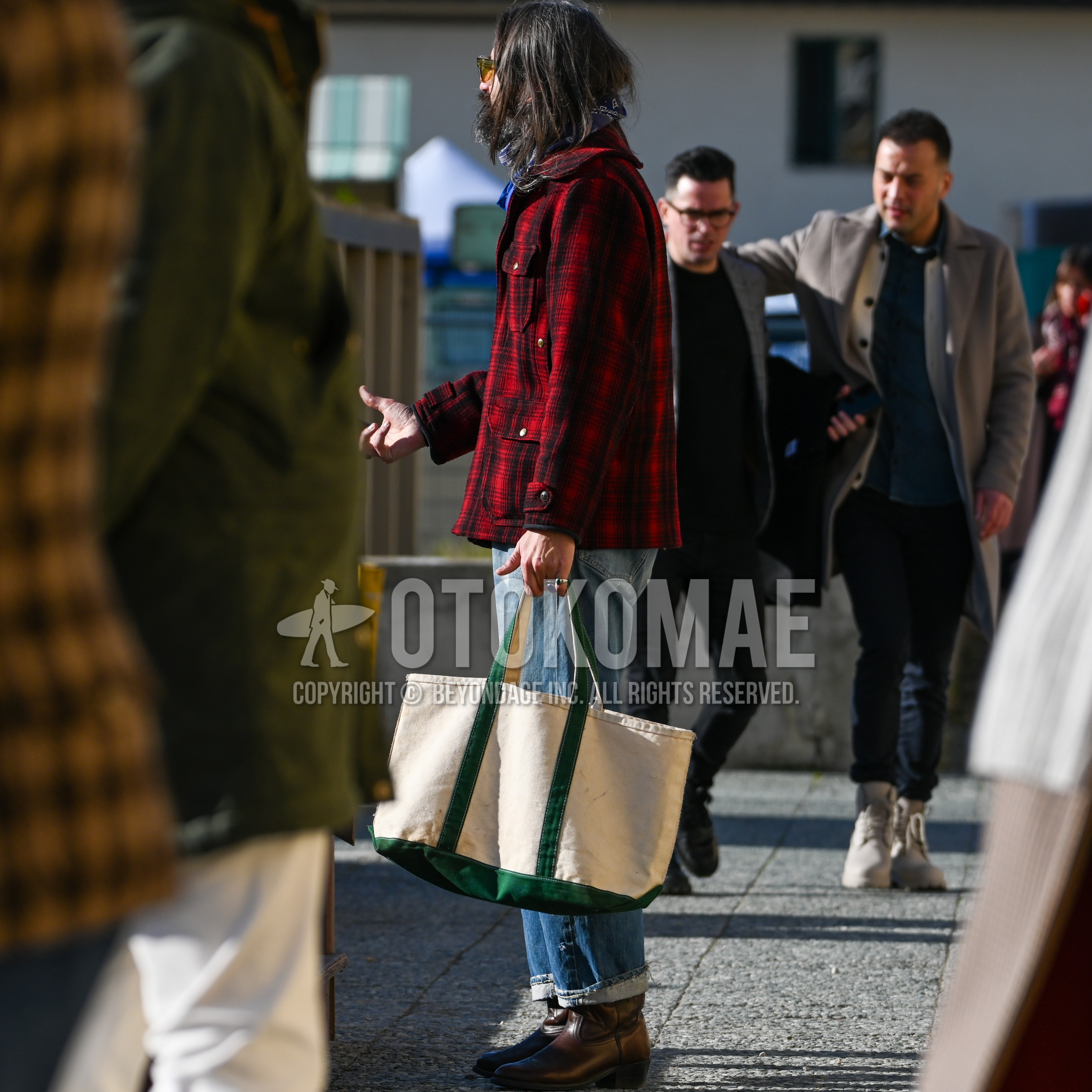 Men's autumn winter outfit with clear plain sunglasses, blue whole pattern scarf, red plain outerwear, plain damaged jeans, brown  boots, white green bag tote bag.