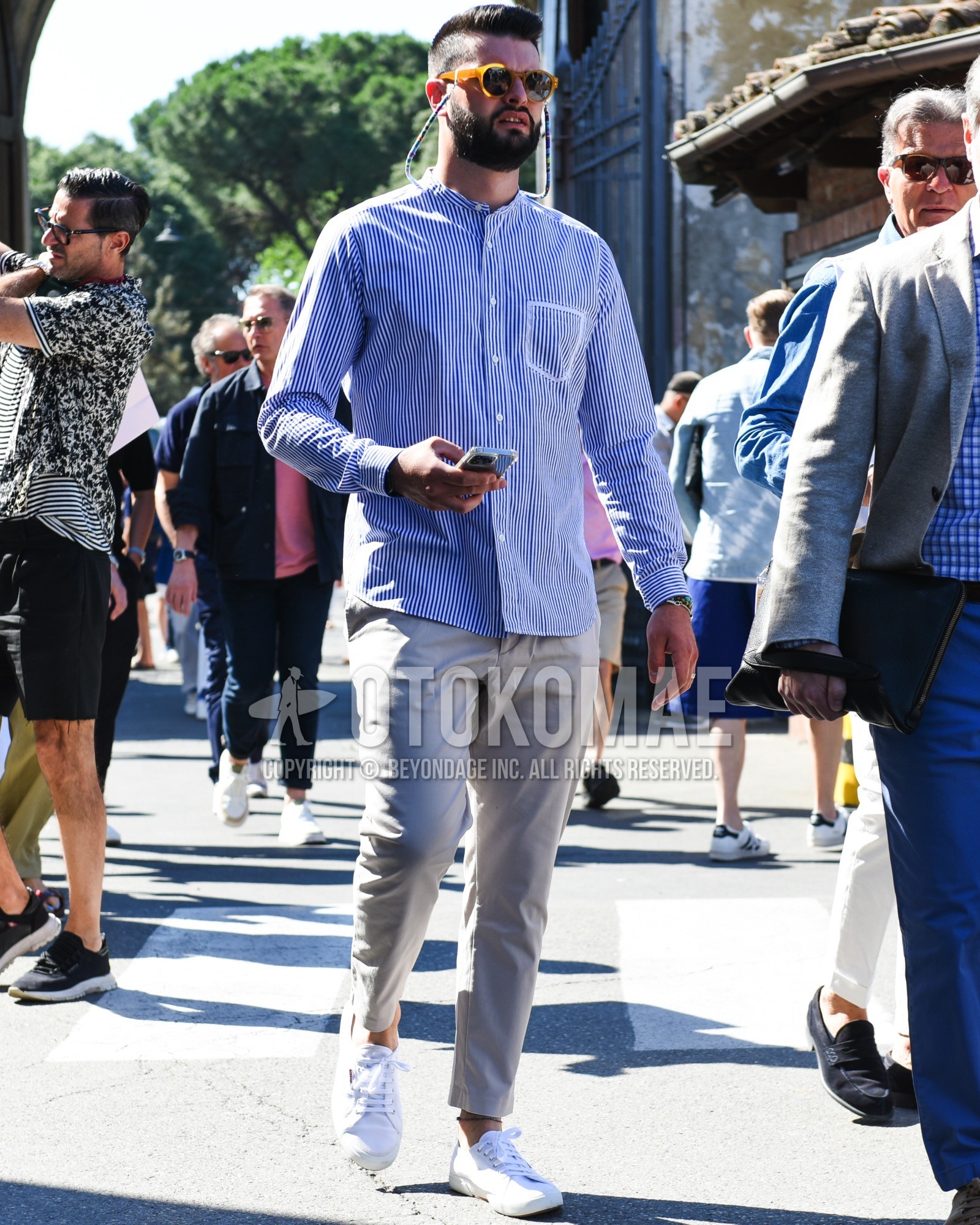 Men's spring summer outfit with yellow plain sunglasses, navy white stripes shirt, gray plain chinos, white low-cut sneakers.