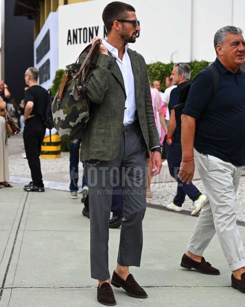 黒無地のサングラス、グリーン無地のテーラードジャケット、白無地のシャツ、グレー無地のベルトレスパンツ、ブラウンコインローファーの革靴、オリーブグリーン迷彩のトートバッグを合わせた秋夏春のメンズコーデ・着こなし。