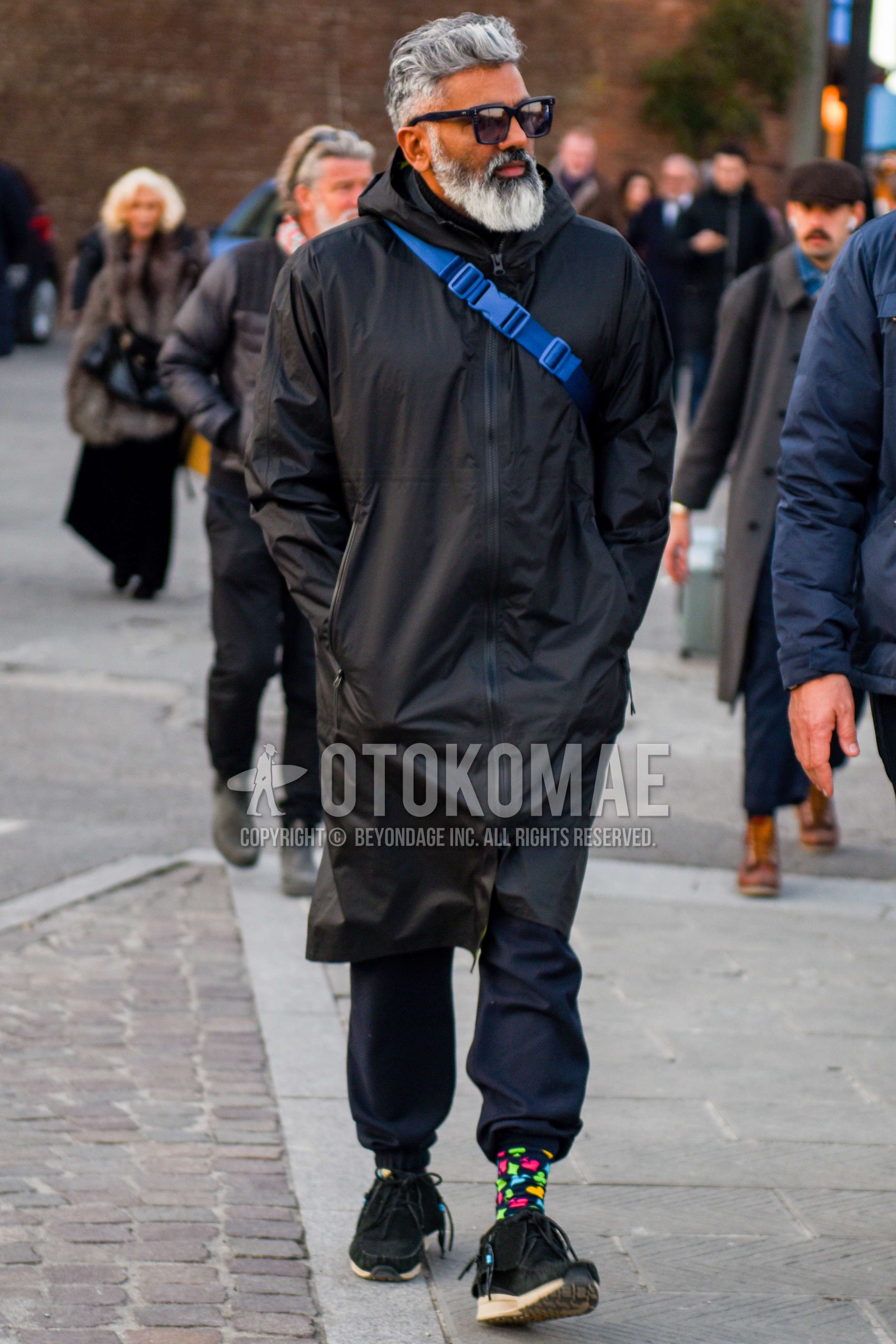 Men's autumn winter outfit with black plain sunglasses, black plain hooded coat, black plain jogger pants/ribbed pants, multi-color socks socks, black  boots, blue plain shoulder bag.