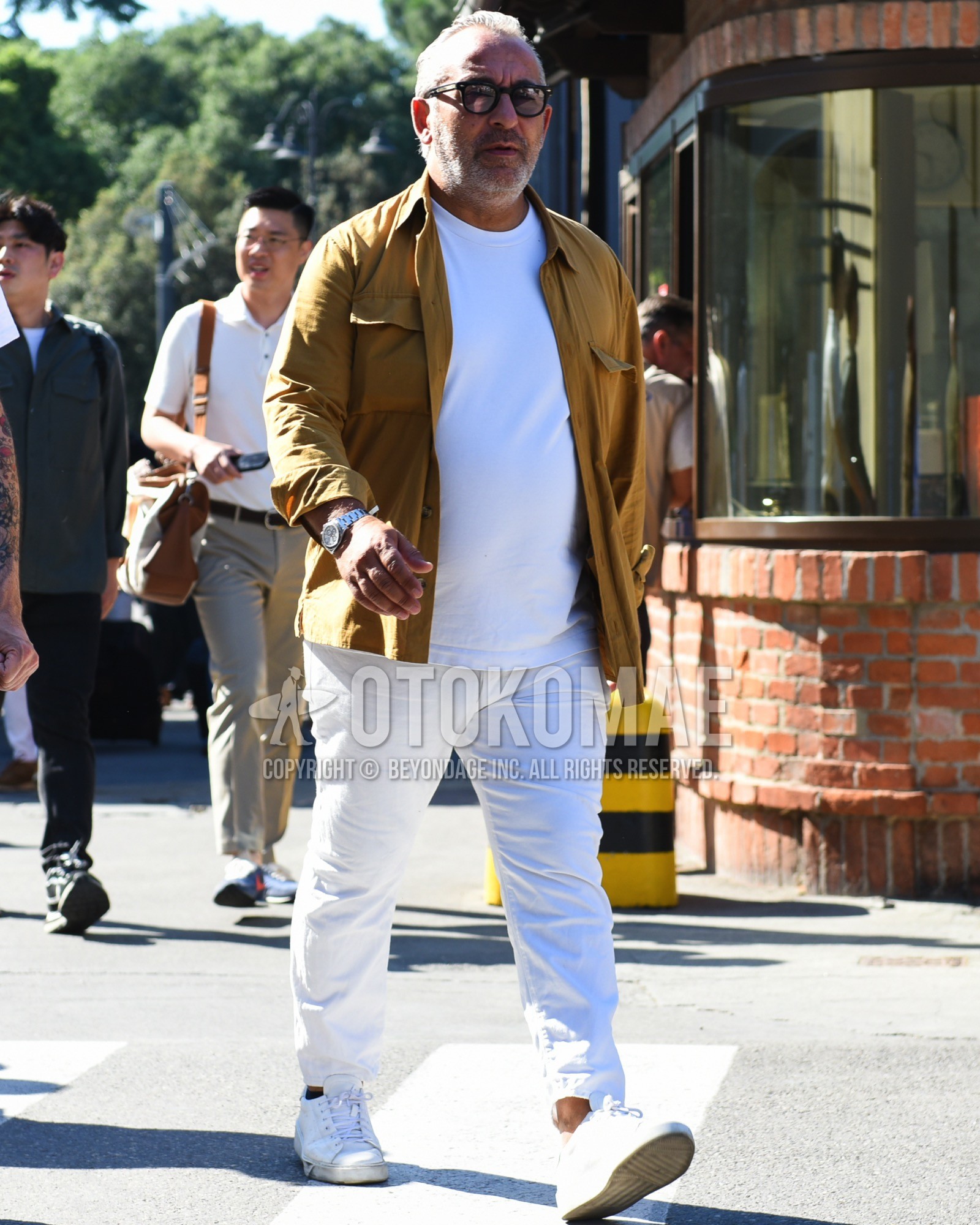 Men's spring summer outfit with black plain glasses, beige plain shirt jacket, white plain t-shirt, white plain cotton pants, white low-cut sneakers.